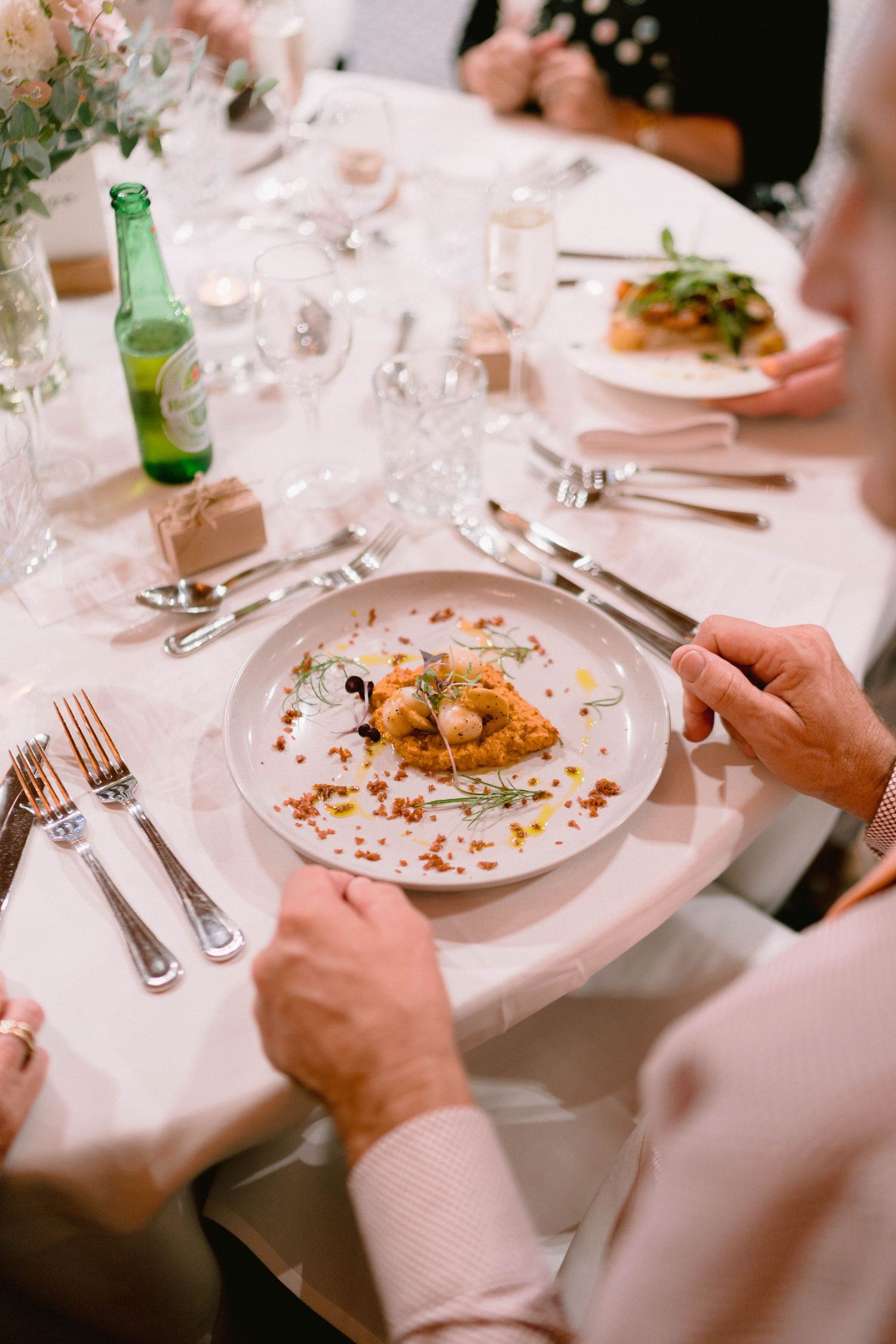 Wedding guests dining at elegant reception tables with white linens and plated meals.