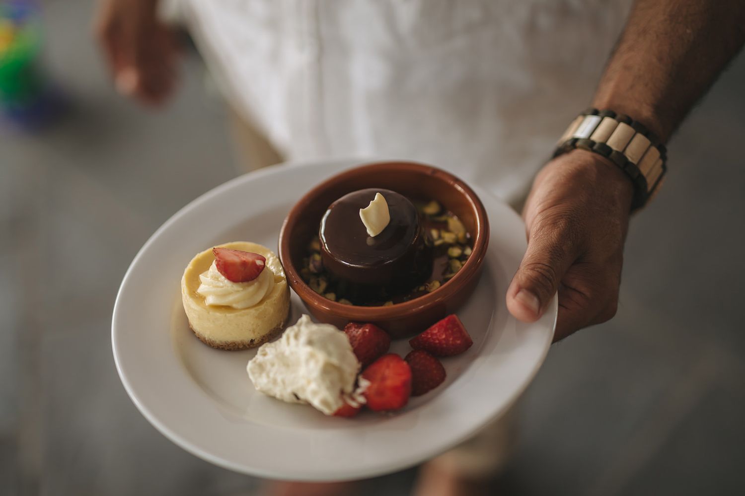 Hands serving chocolate lava cakes on white plates with vanilla ice cream and fresh strawberries.