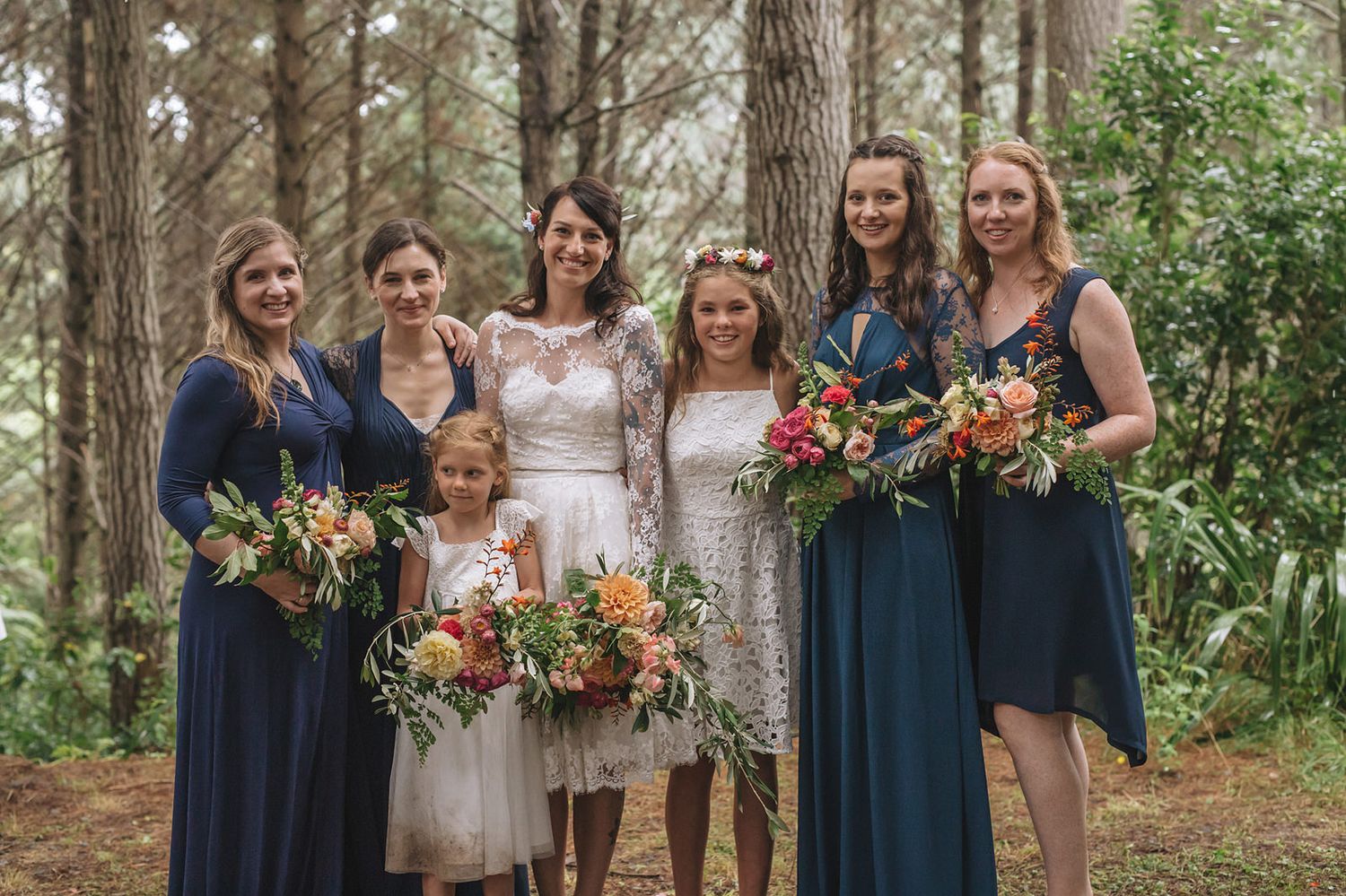 Wedding party in navy blue and white dresses posing together in wooded outdoor setting.