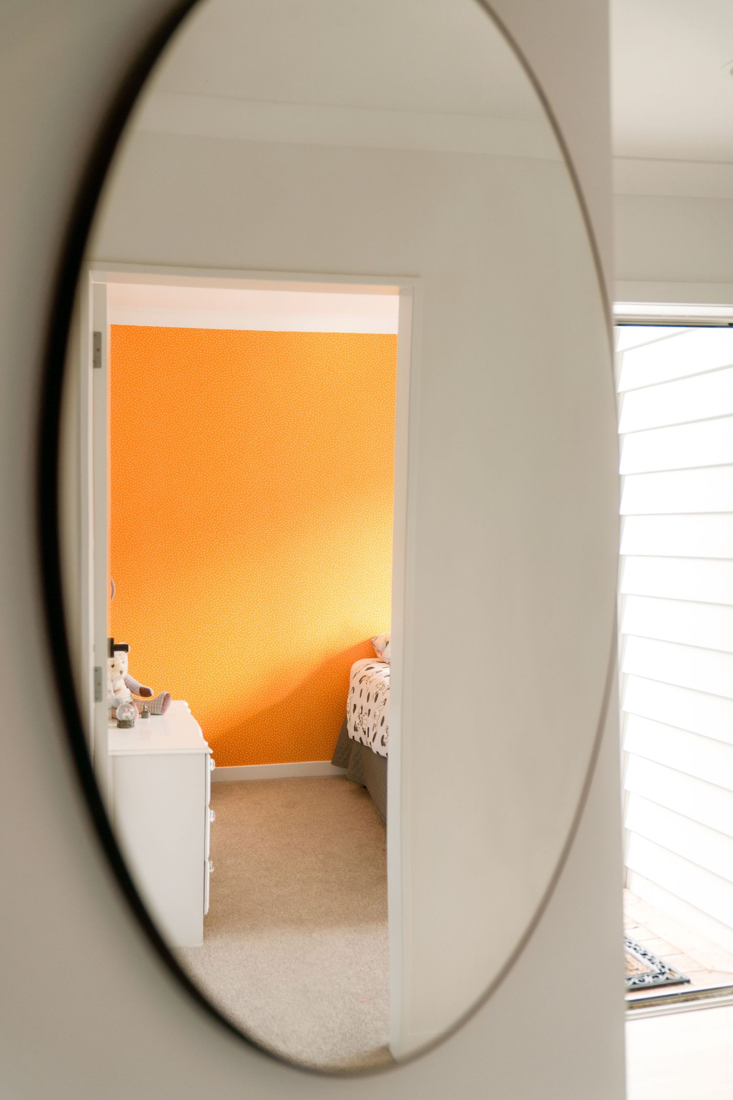 Circular mirror reflecting a vibrant orange accent wall in a carpeted room.