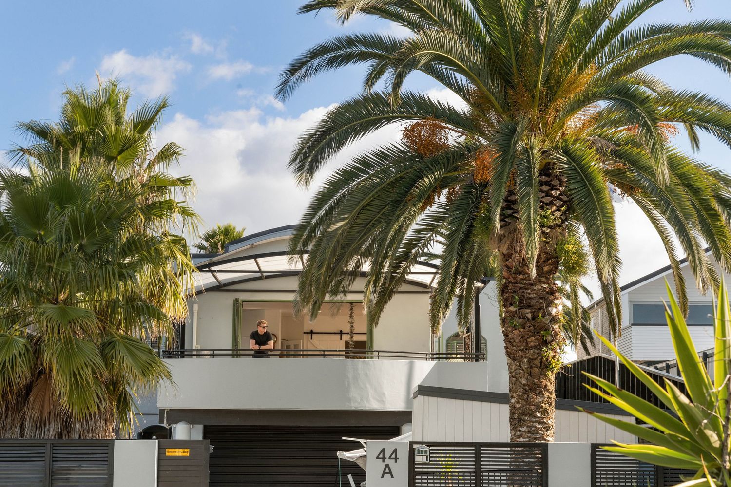 Contemporary beach house with tall palm trees and modern architectural features against blue sky.