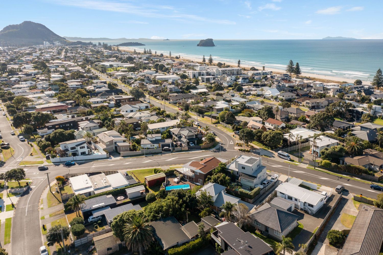 Aerial panoramic view of Mount Maunganui beach town with ocean, mountains, and coastal buildings in New Zealand.
