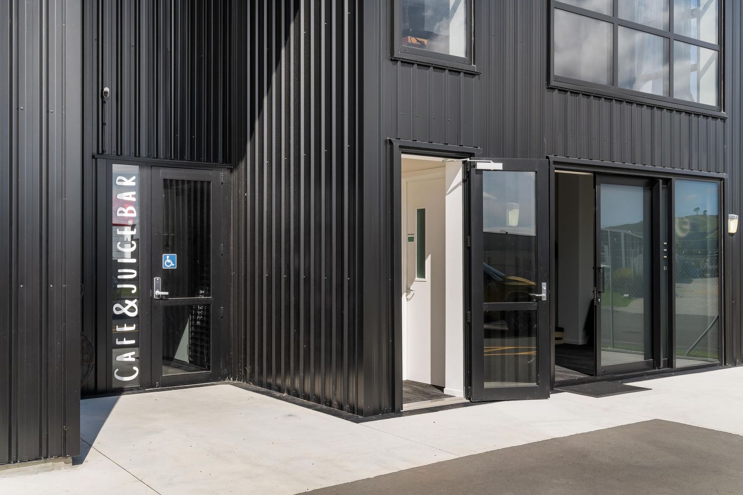 Modern black commercial building exterior with vertical metal siding and glass entry doors.
