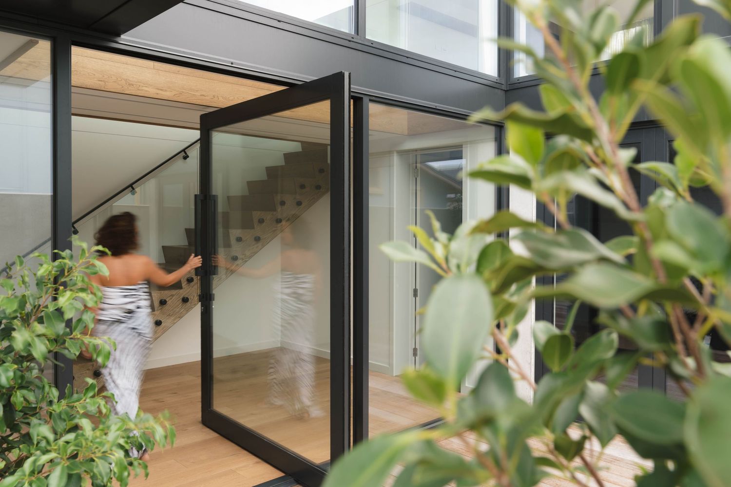 Contemporary glass doors and windows with black frames surrounded by lush greenery.