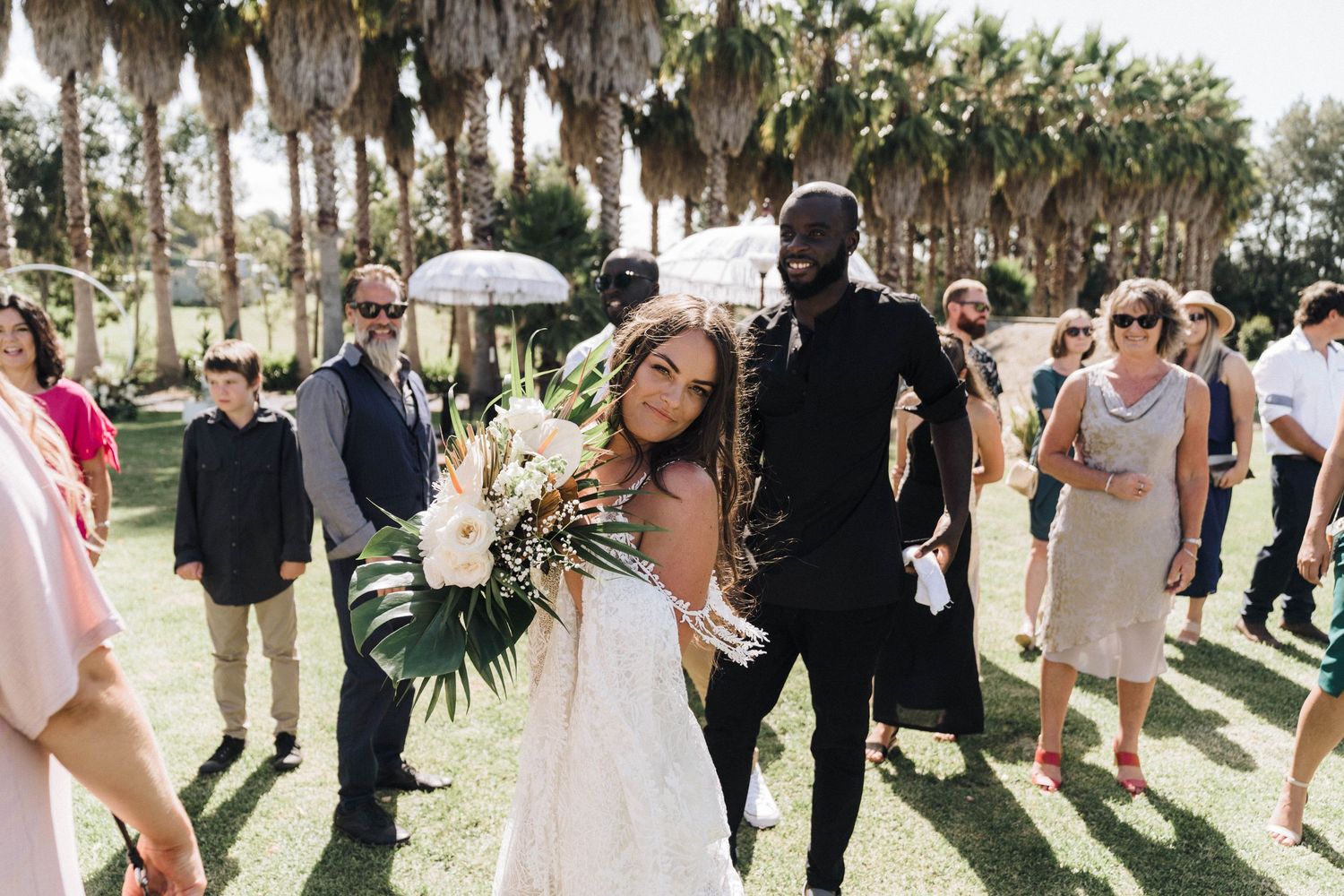 A wedding celebration on a sunny lawn lined with palm trees.