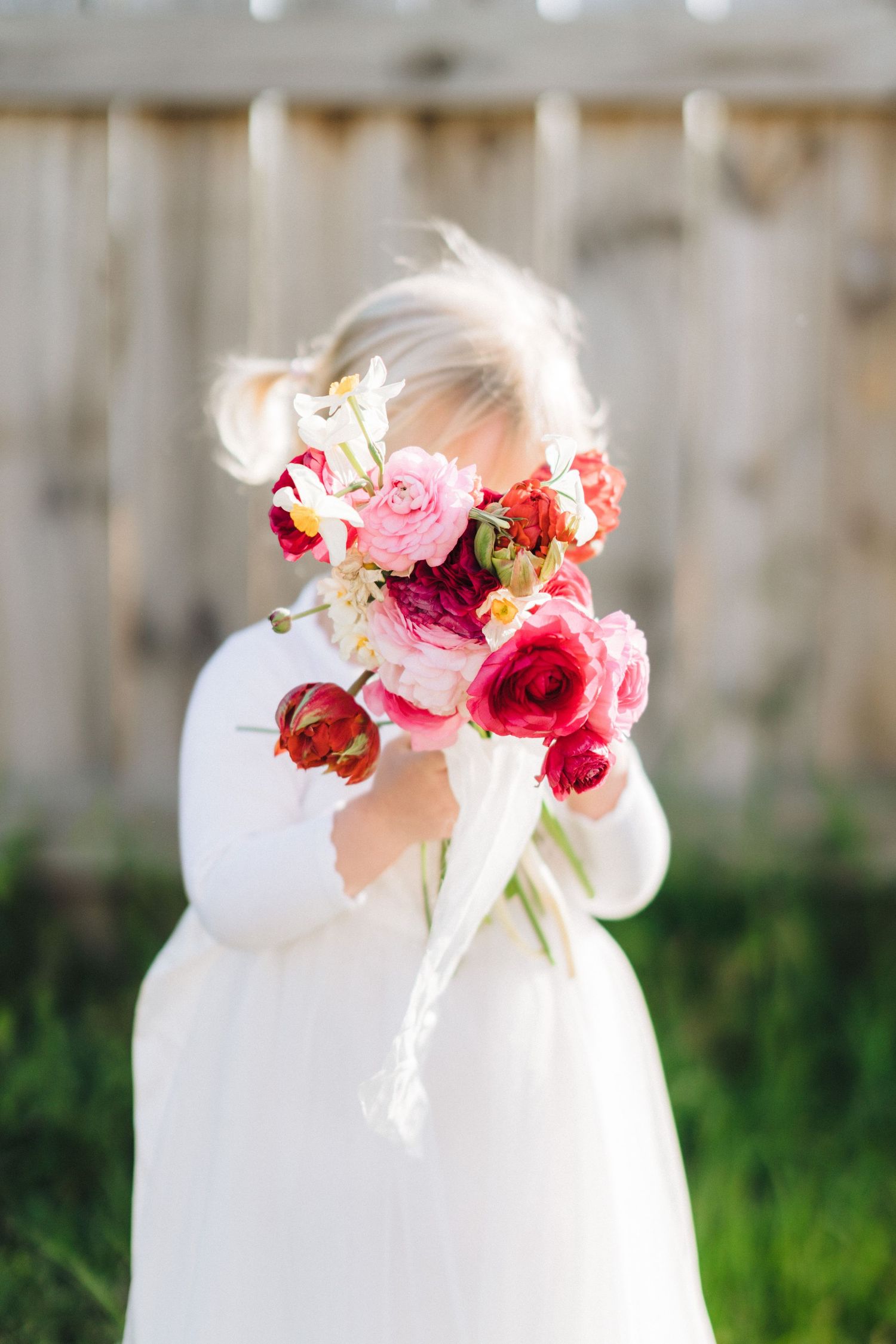 A beautiful bouquet of pink and red roses held in front of white dress.