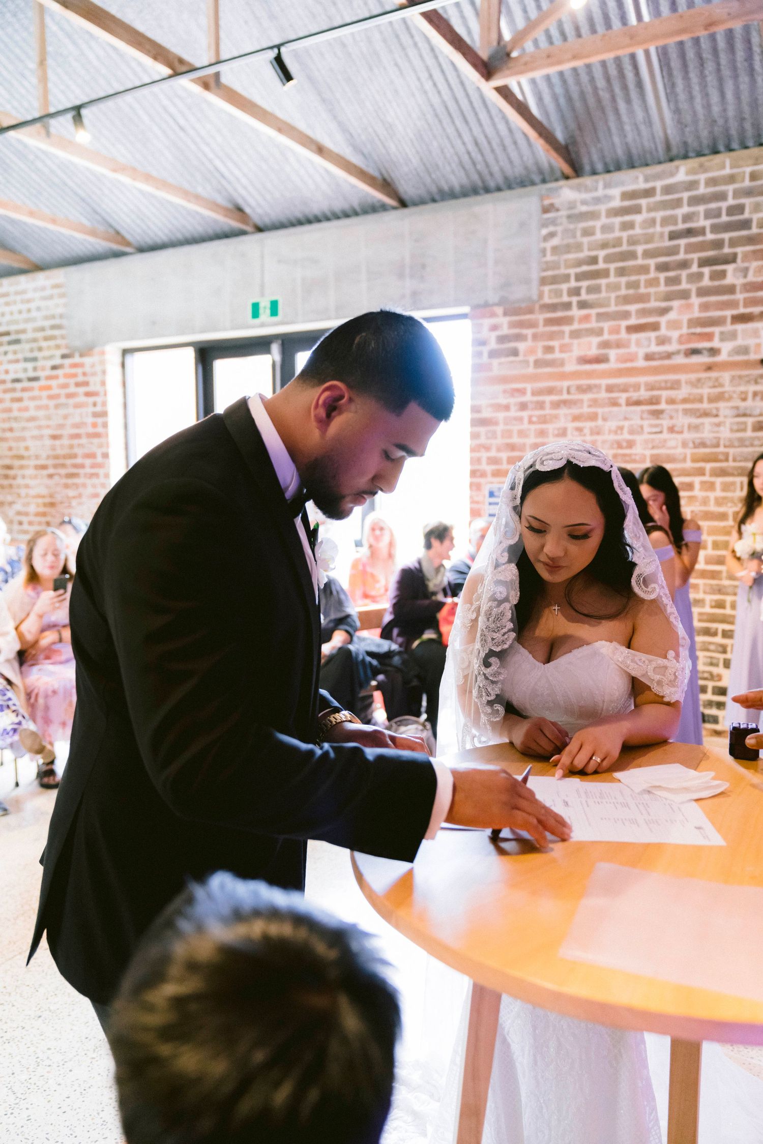 A couple signs their marriage certificate at a wooden table during their wedding ceremony.