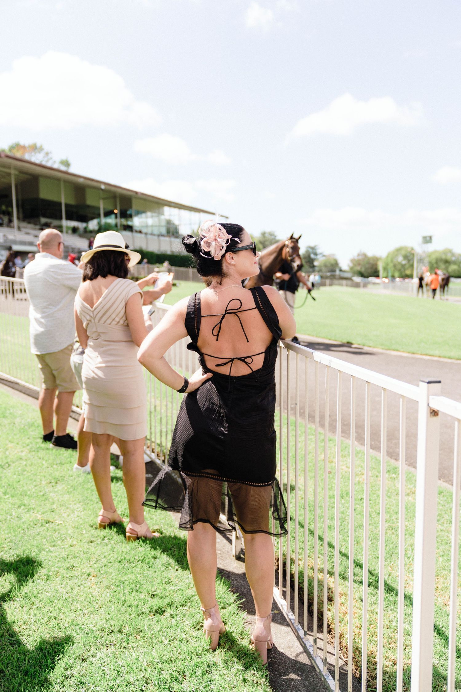 Group of people leaning on racetrack railing during a sunny day at the races.