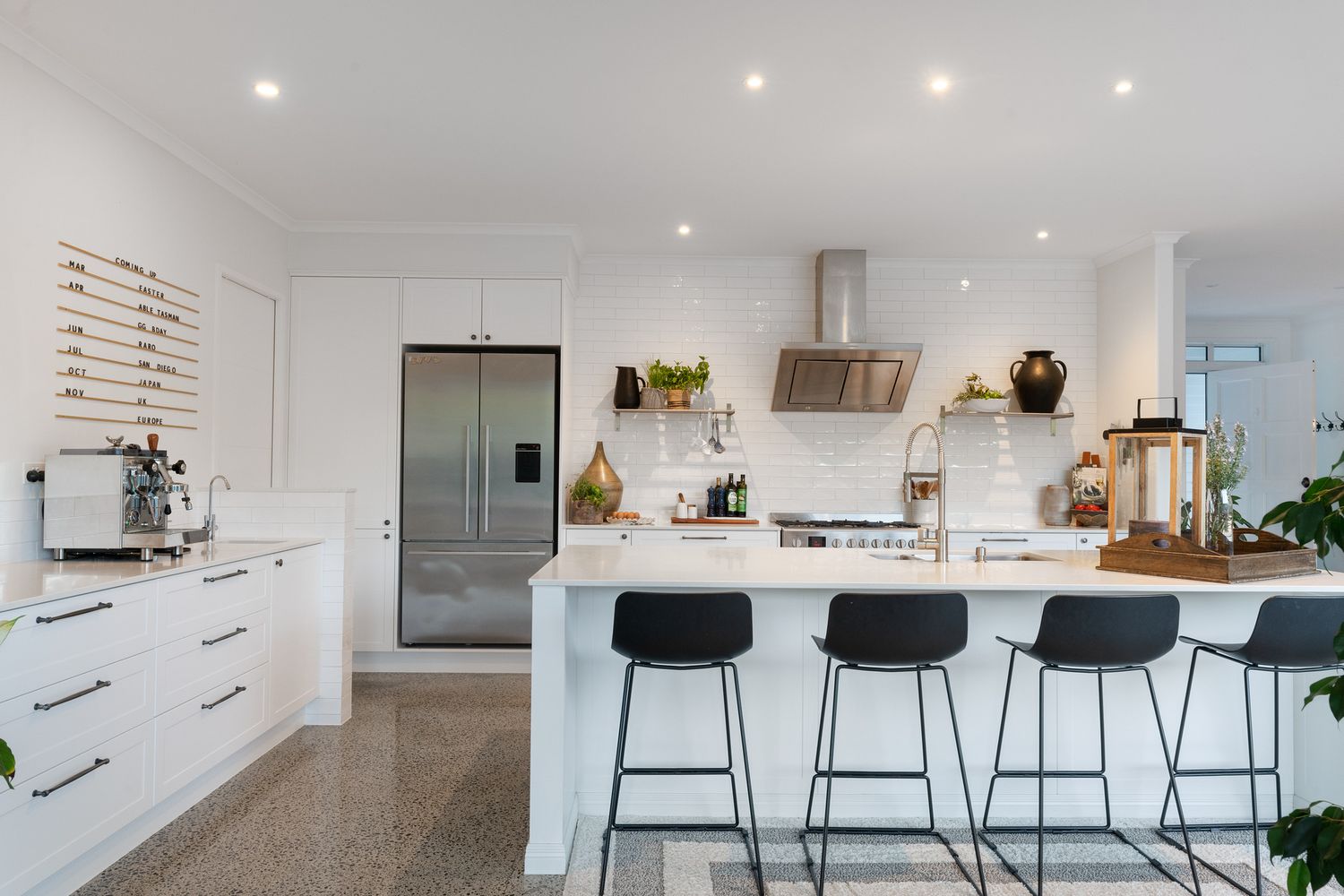 Sleek white kitchen with black bar stools, stainless steel appliances and wooden accents.