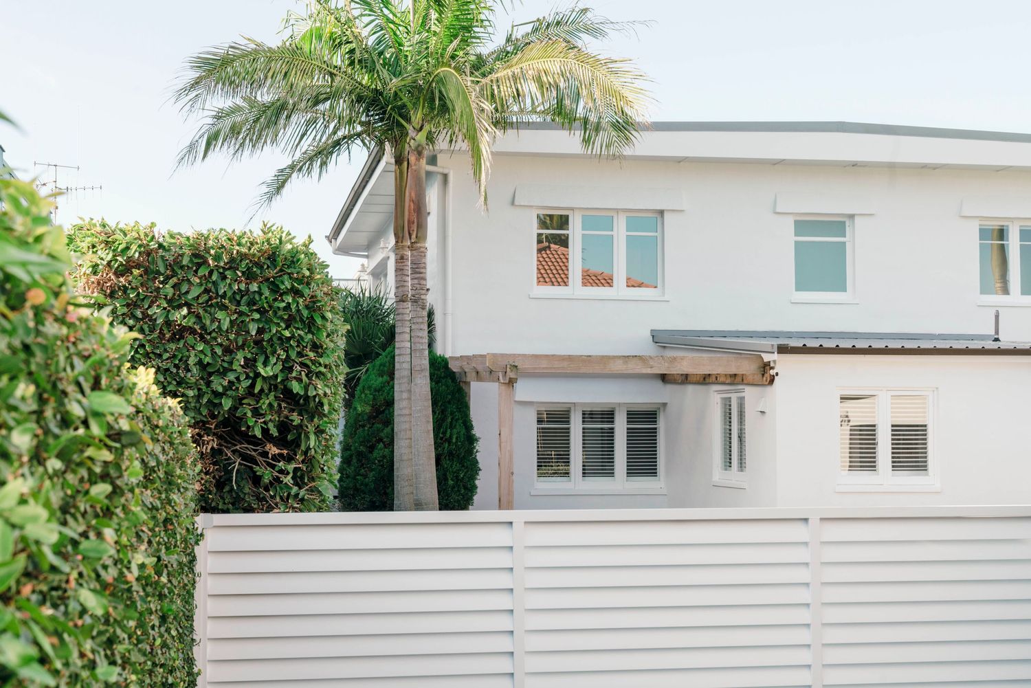 Modern white beach house exterior with palm trees and sleek architectural design.