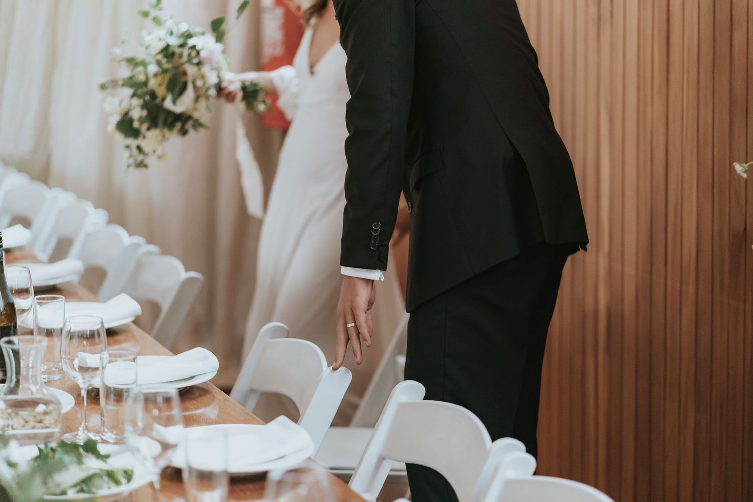 Place setting at an elegant wedding reception with white folding chairs and wooden wall paneling.