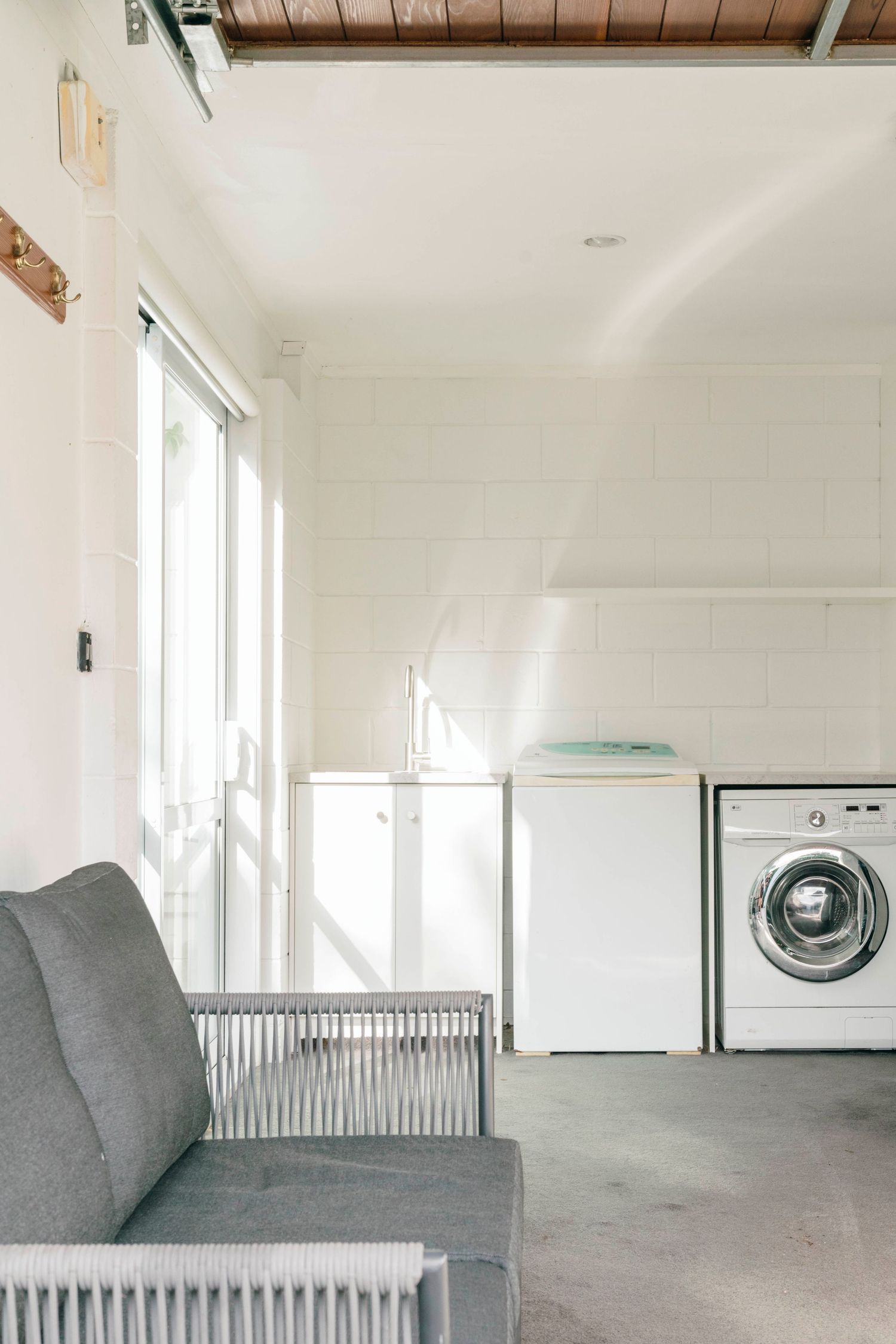 Laundry room with gray sofa, washer and dryer units, and exposed wooden ceiling beams.