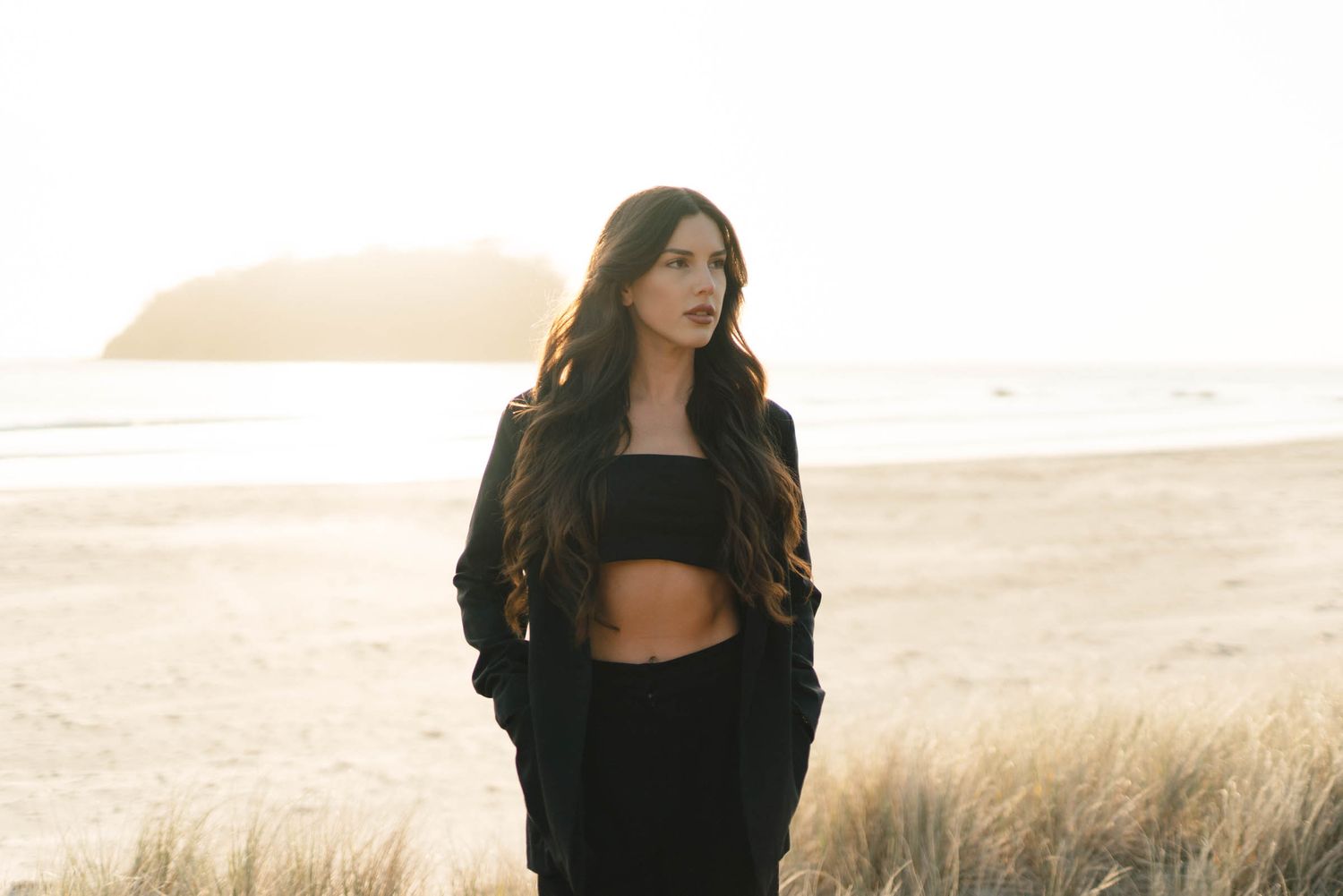 A person stands in tall grass field at sunset creating a serene outdoor portrait silhouette effect.