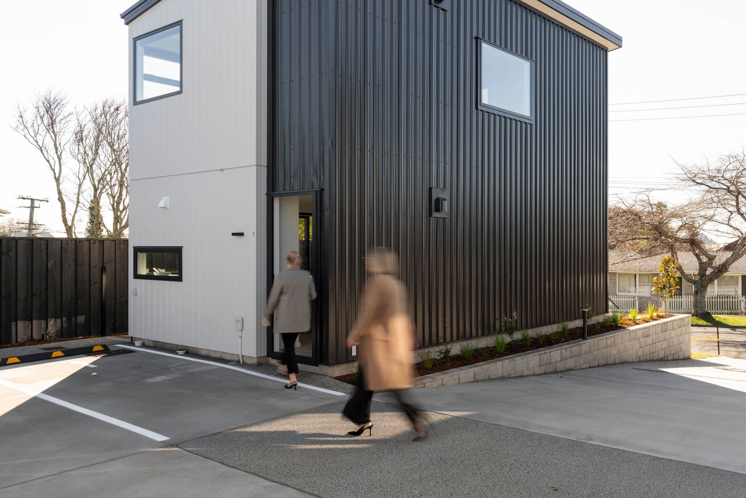 Modern tiny house exterior features contrasting black metal siding and white stucco with two people entering through a doorway.