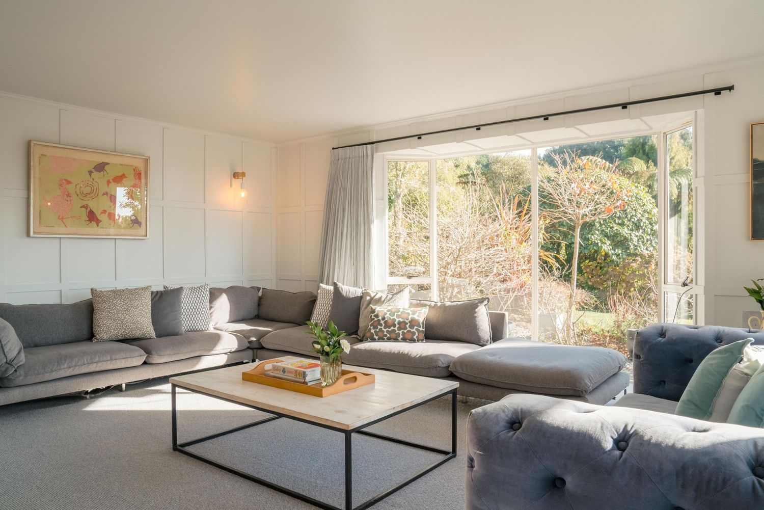 Modern living room with large sectional sofa, coffee table and bright window overlooking natural scenery.