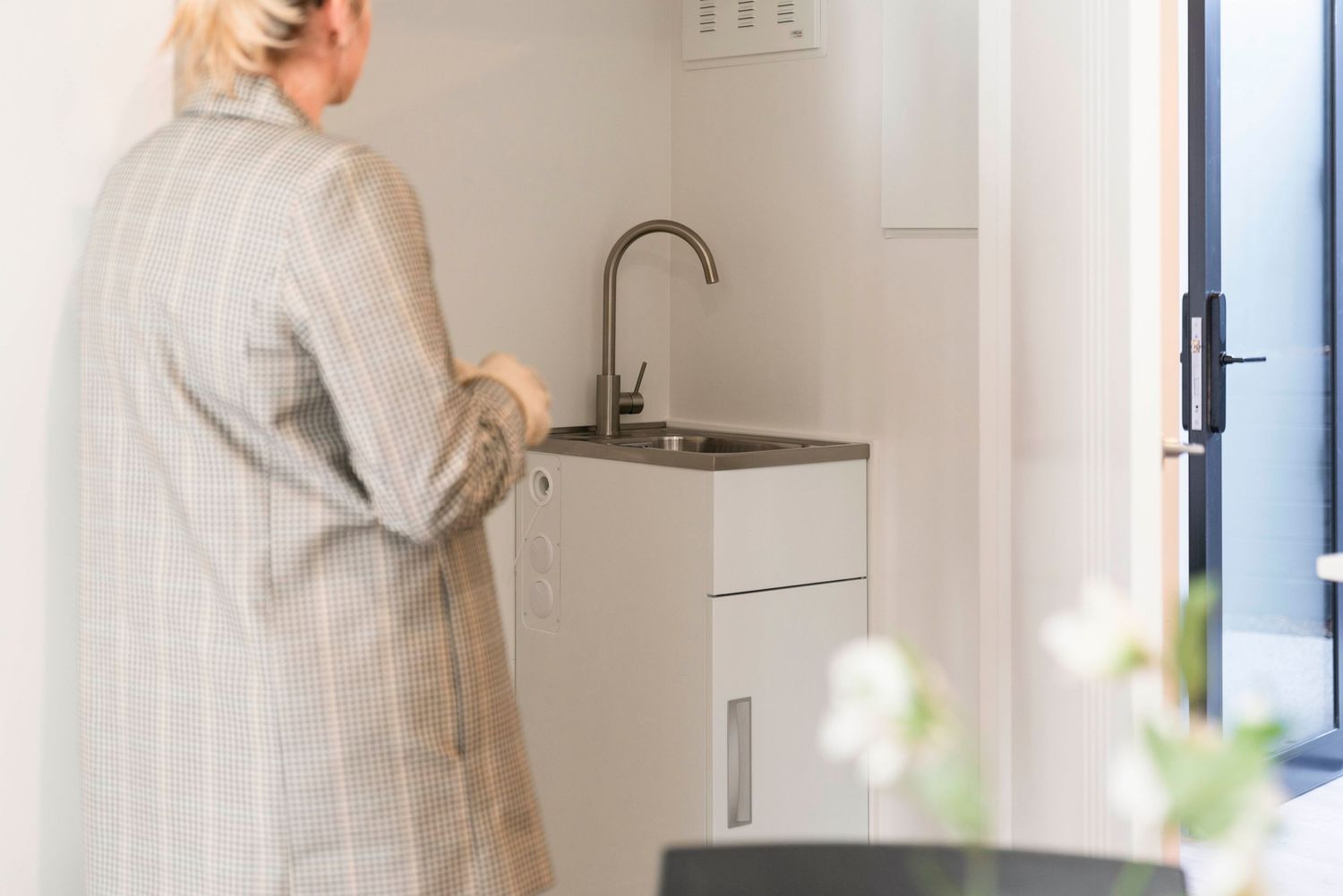 Person in a striped bathrobe washing hands at a modern white sink in a bright, minimalist bathroom interior.