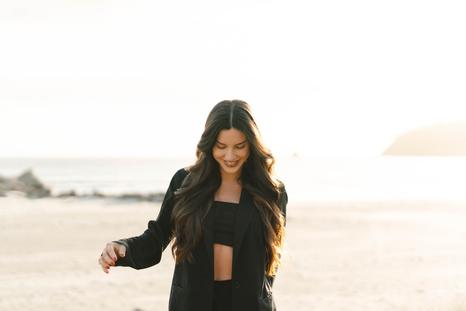 A person wearing black clothing laughs while posing in warm sunlight outdoors.
