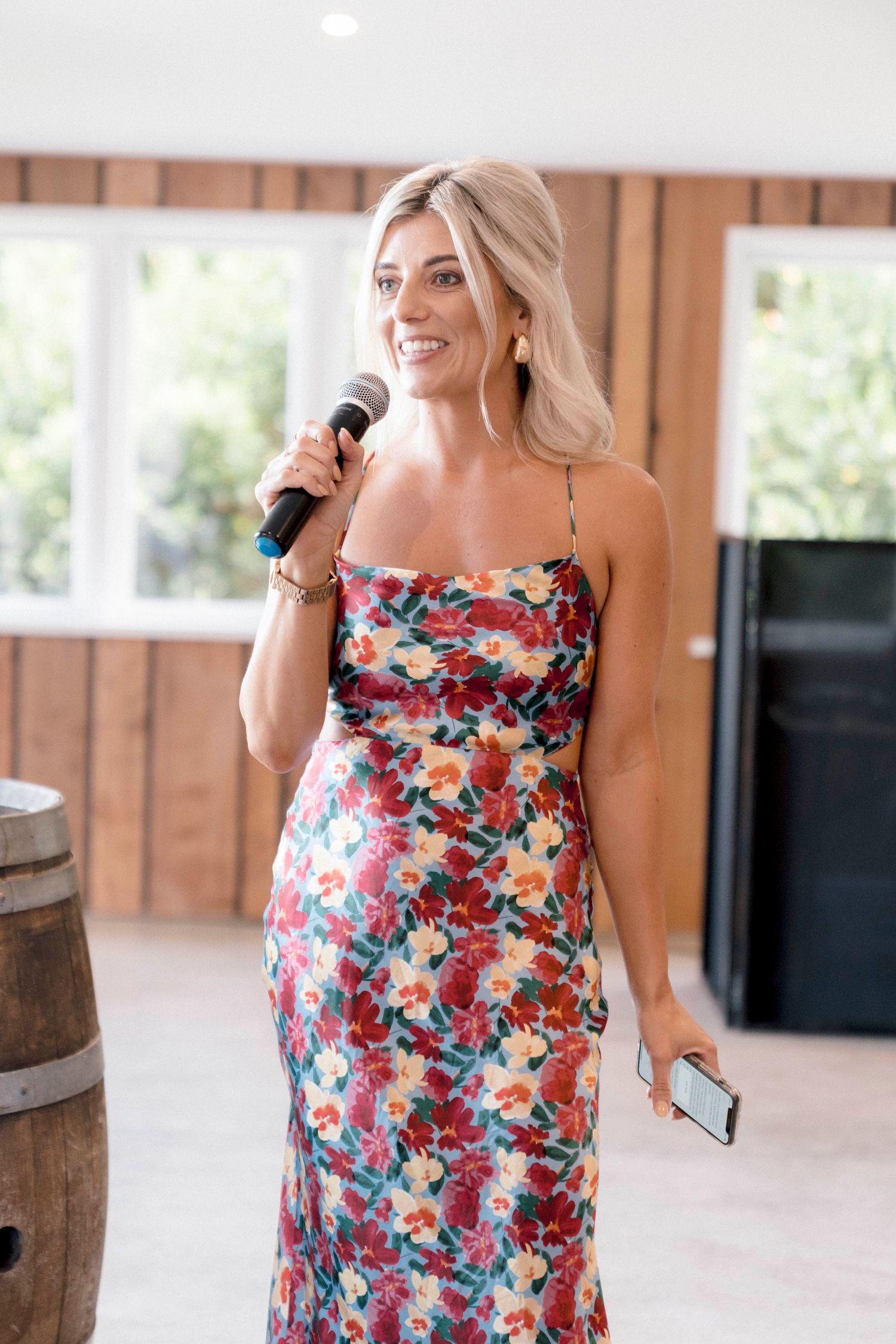 Person in a colorful floral dress holds microphone during an indoor event with wooden wall panels.