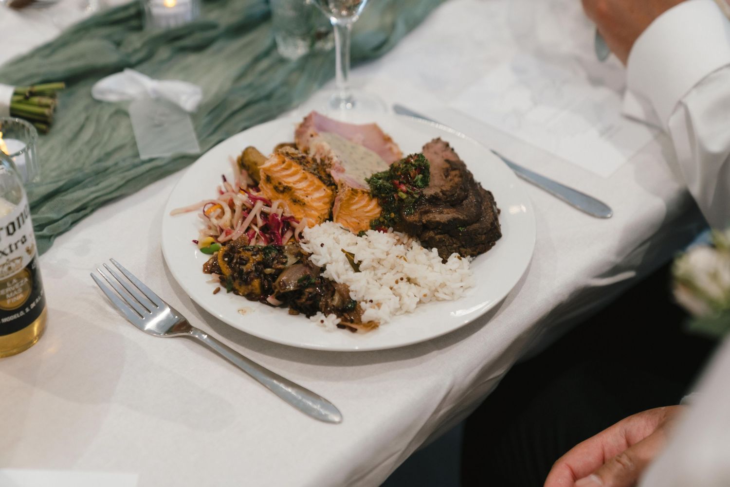 Wedding reception dinner plates with rice and meat dishes on white tablecloths.