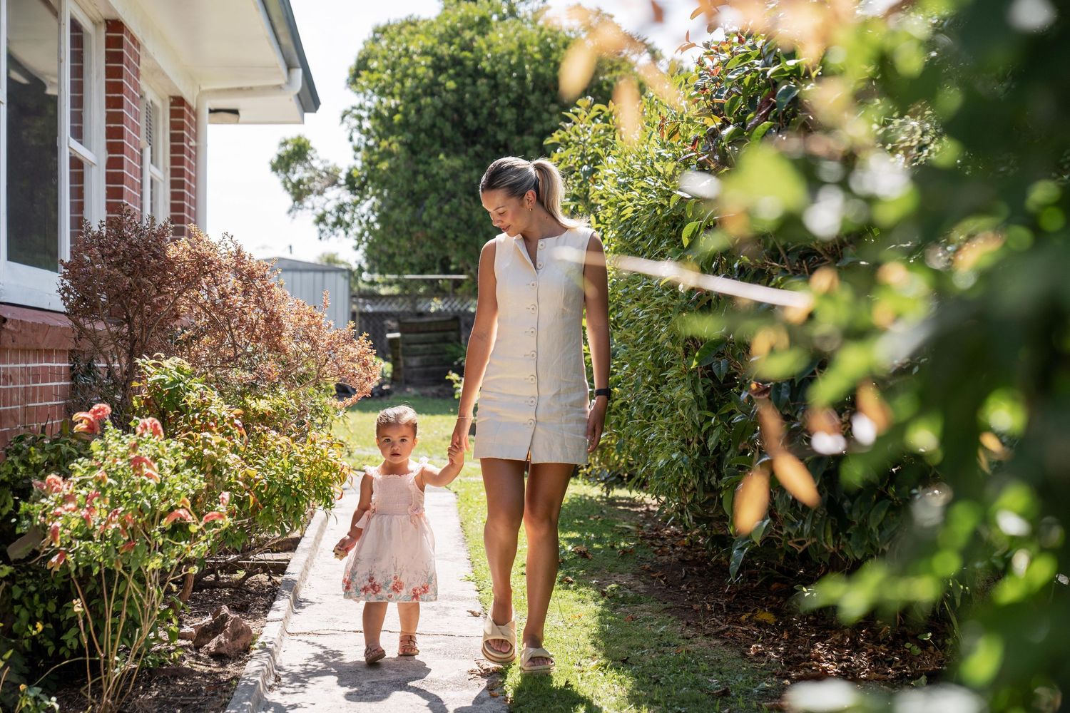 Walking together along a garden path beside a brick home on a bright summer day.