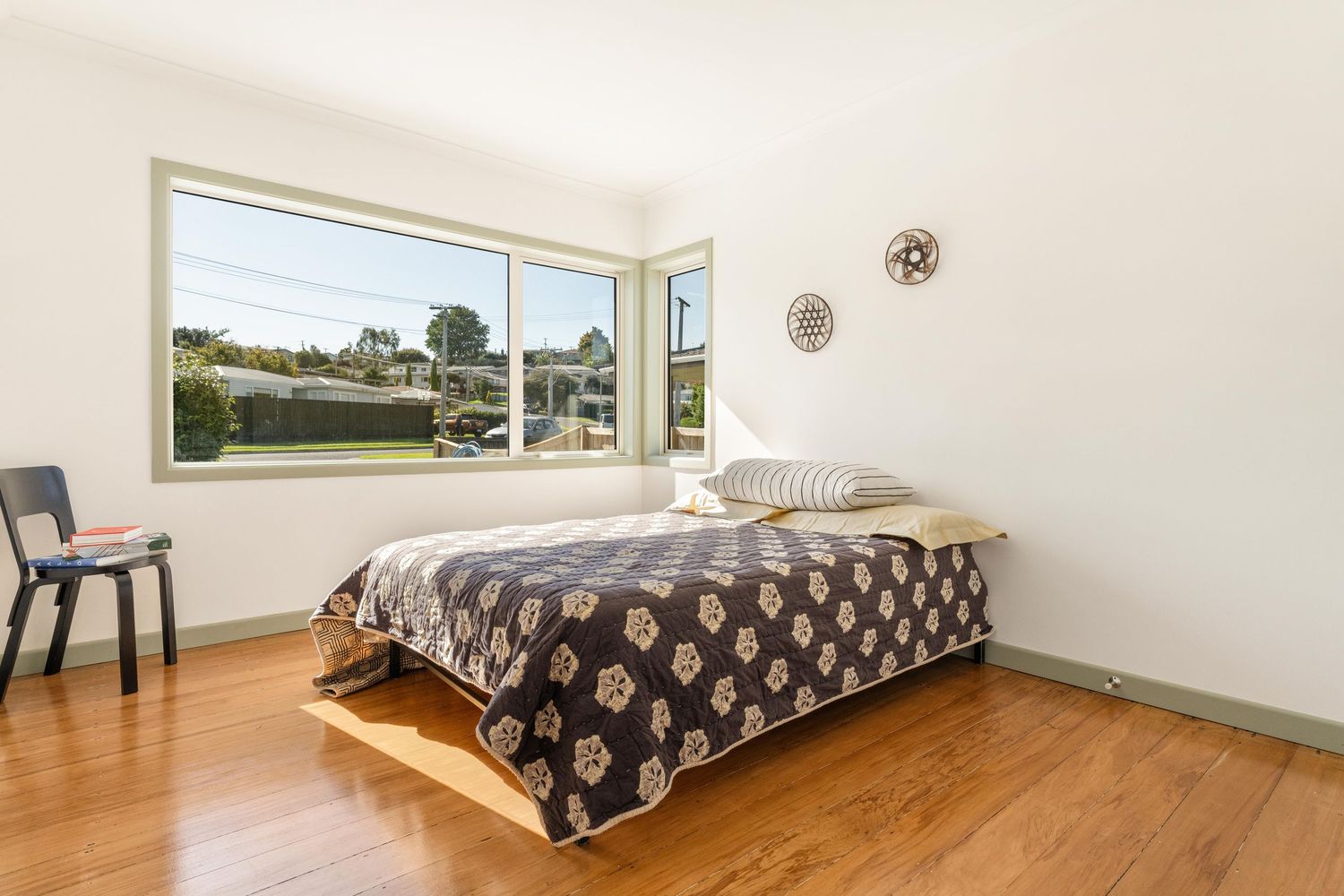 Airy bedroom featuring patterned bedspread, hardwood floors and corner windows with scenic views.