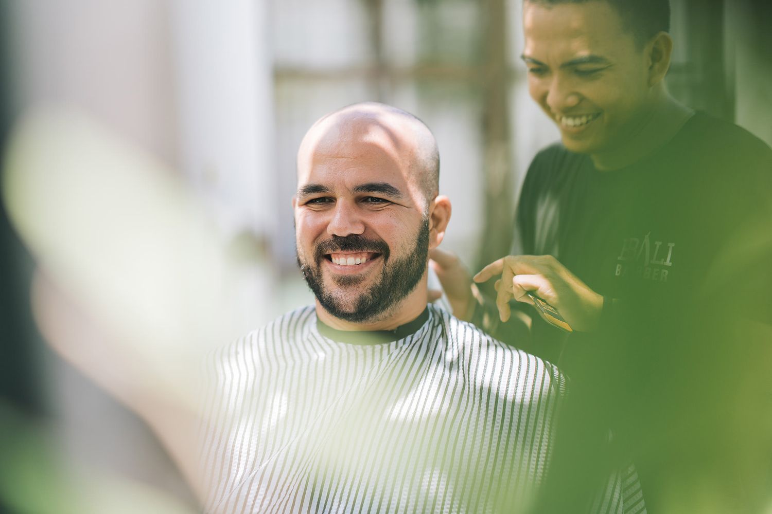 Men smiling through green foliage in outdoor setting.