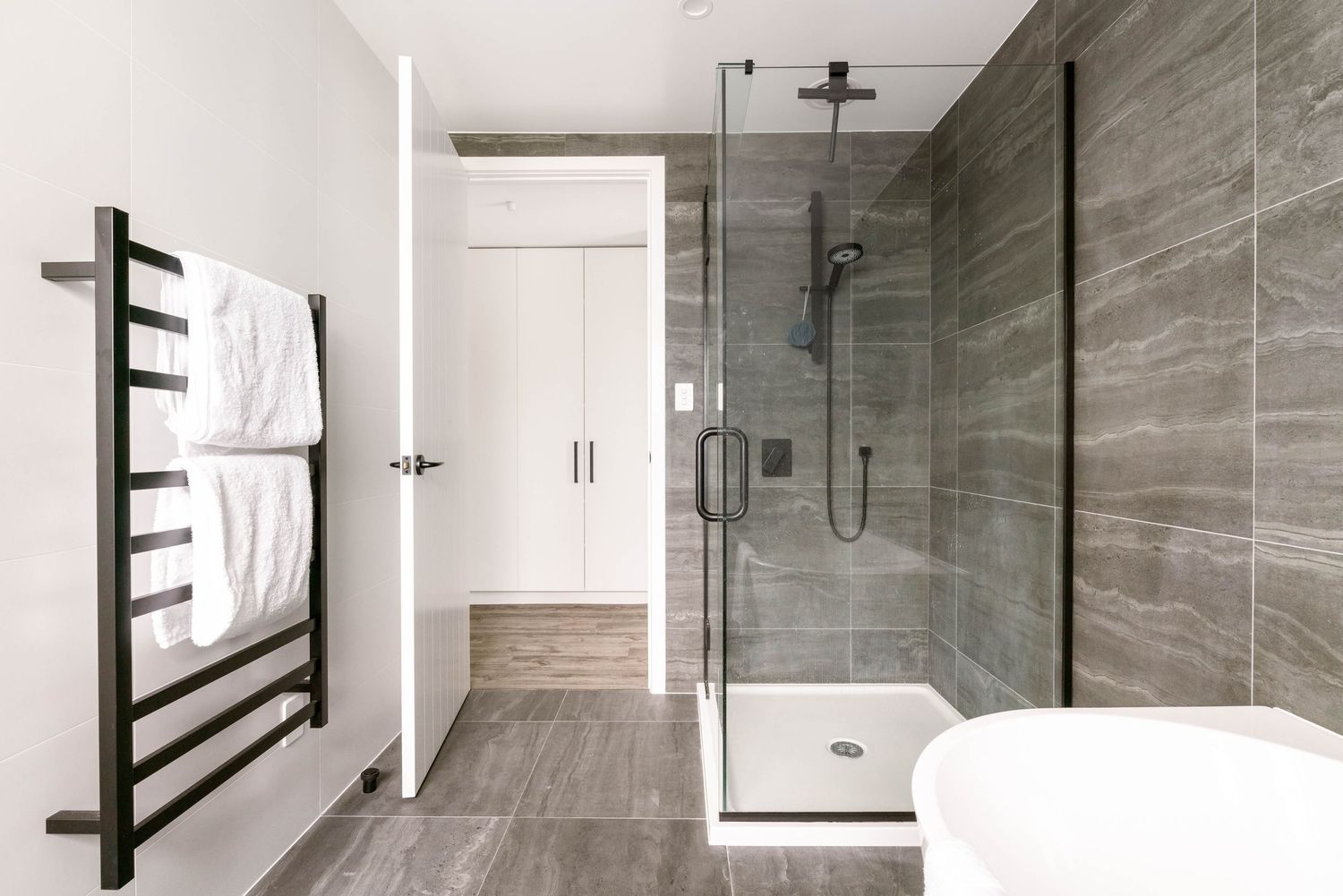 Modern bathroom with gray tile, glass shower enclosure, and black heated towel rail in minimalist design.