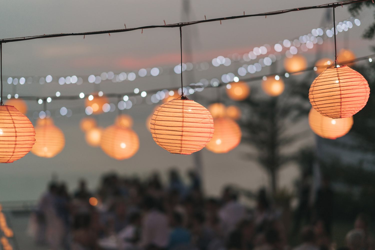 String of glowing orange paper lanterns hanging outdoors at dusk creating a warm ambient atmosphere.