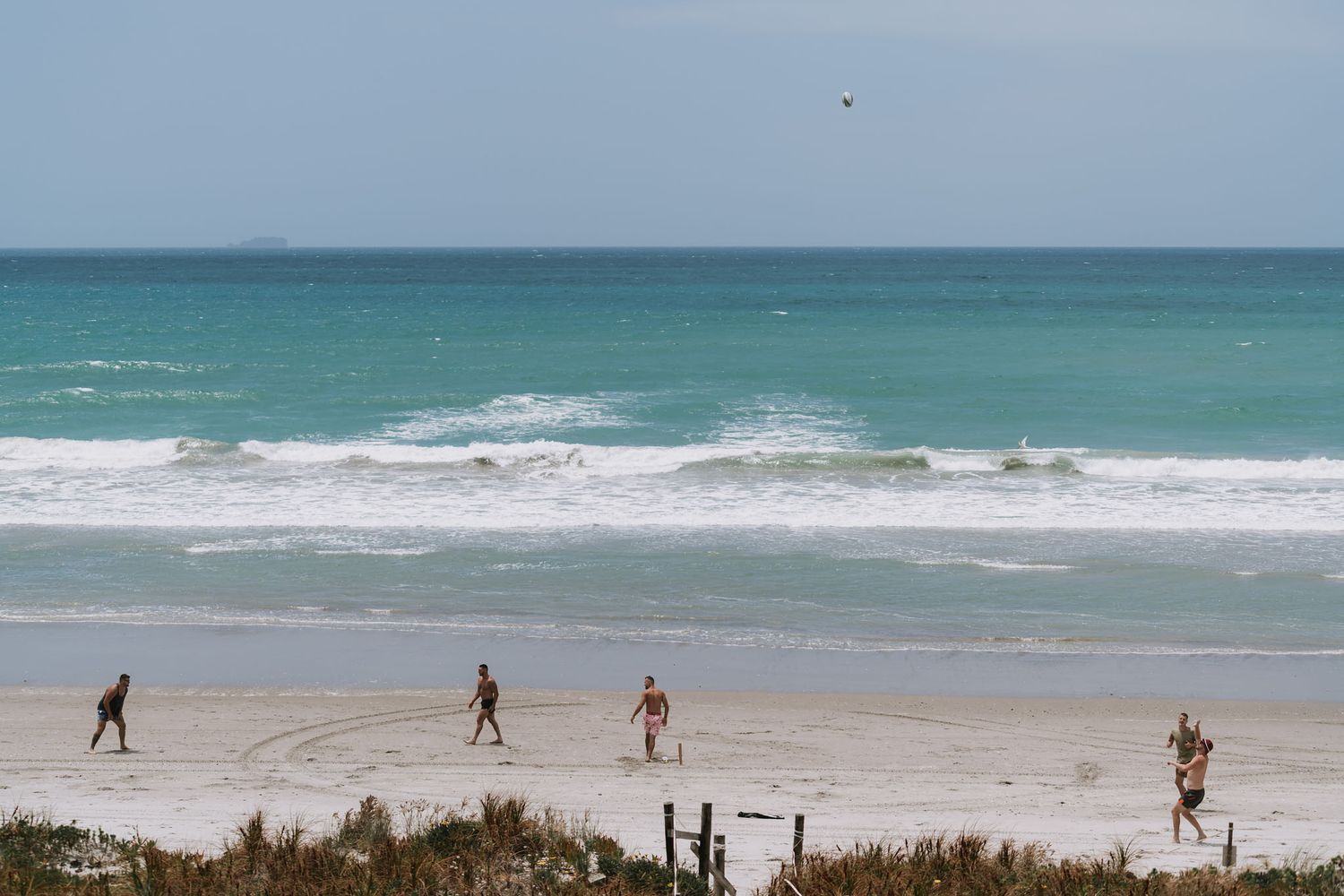 Beachgoers walk along a sandy shore with turquoise waves crashing on a sunny day at a tropical beach.