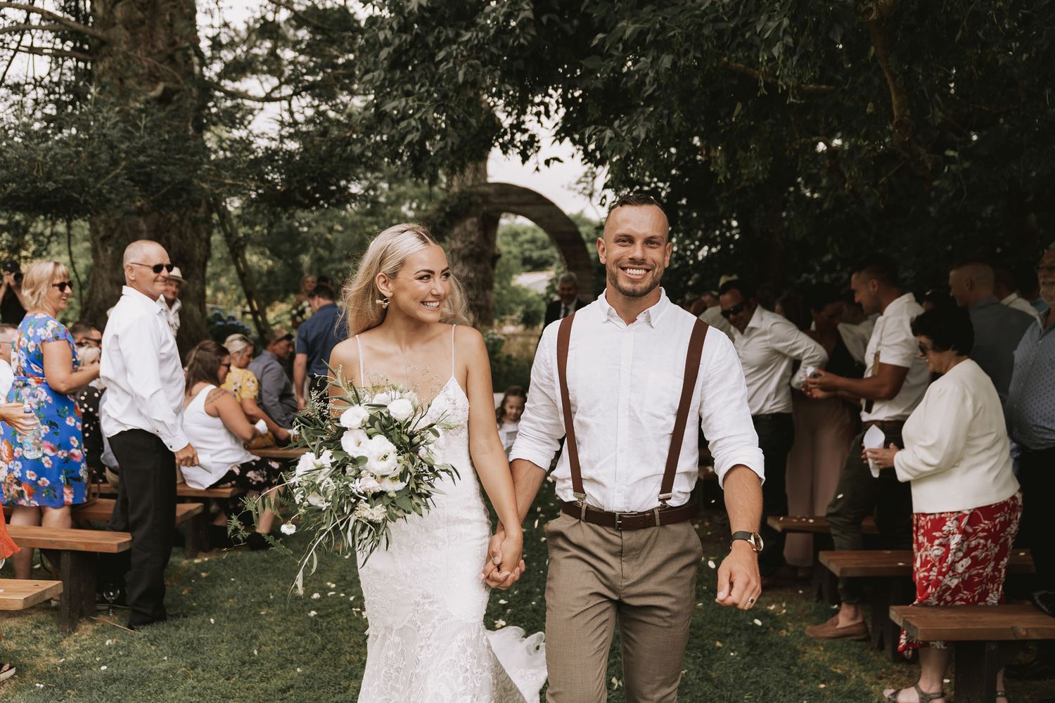 People gather outdoors at a rustic wedding celebration with warm lighting and natural decor throughout the venue.
