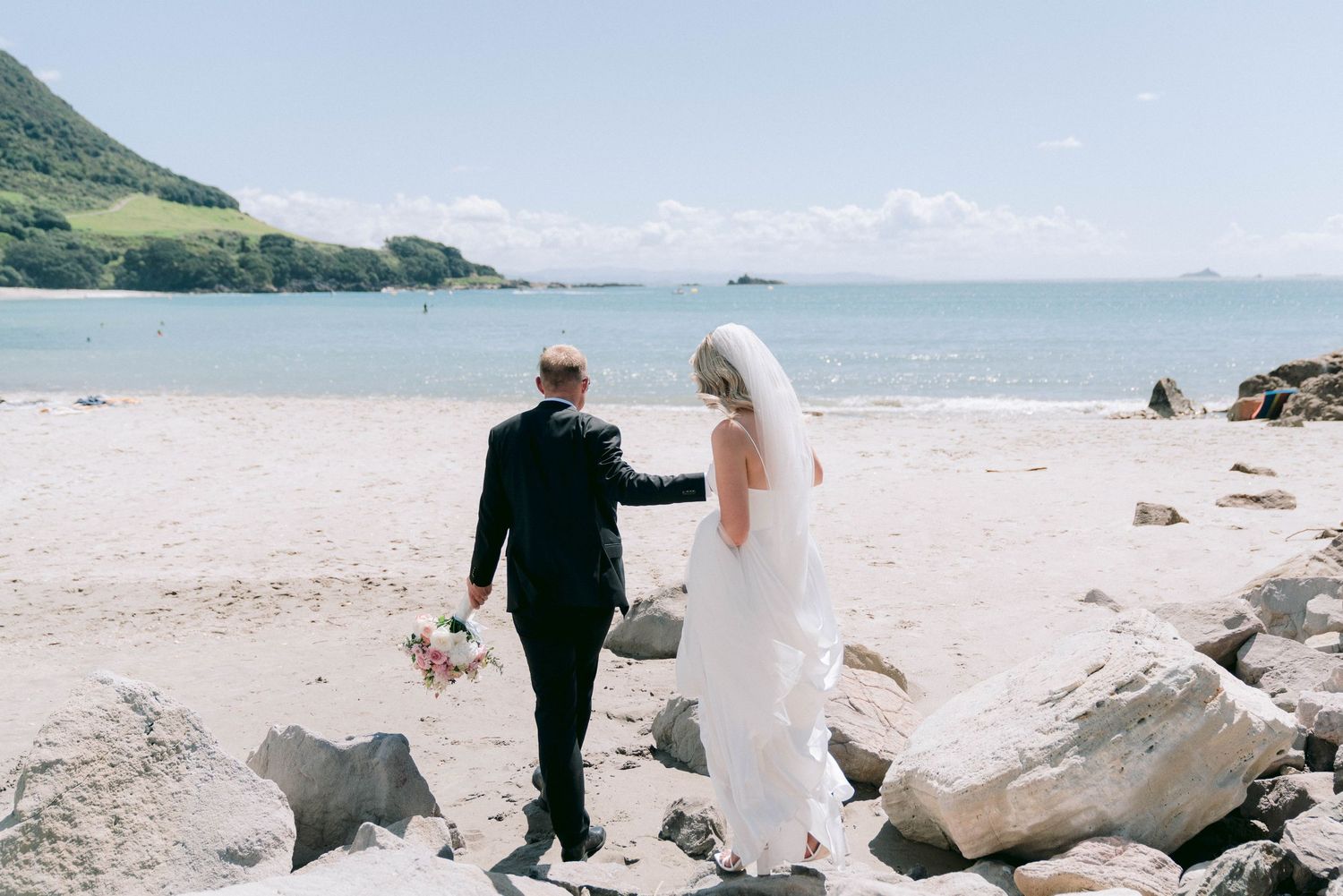 Wedding couple posing on a scenic beach with large rocks and ocean views in the background.