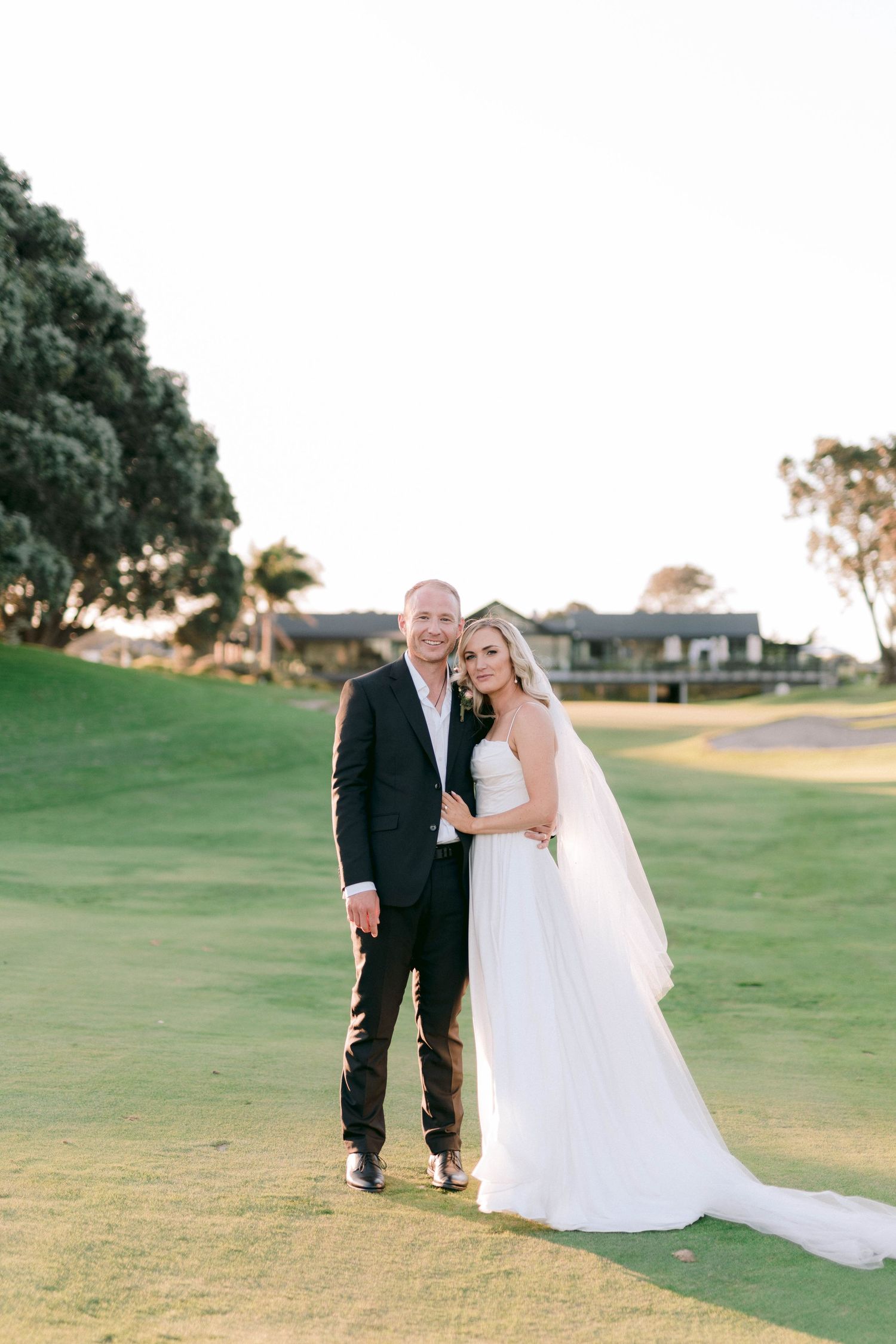 A couple dances together on a green lawn at sunset during a joyous wedding celebration.