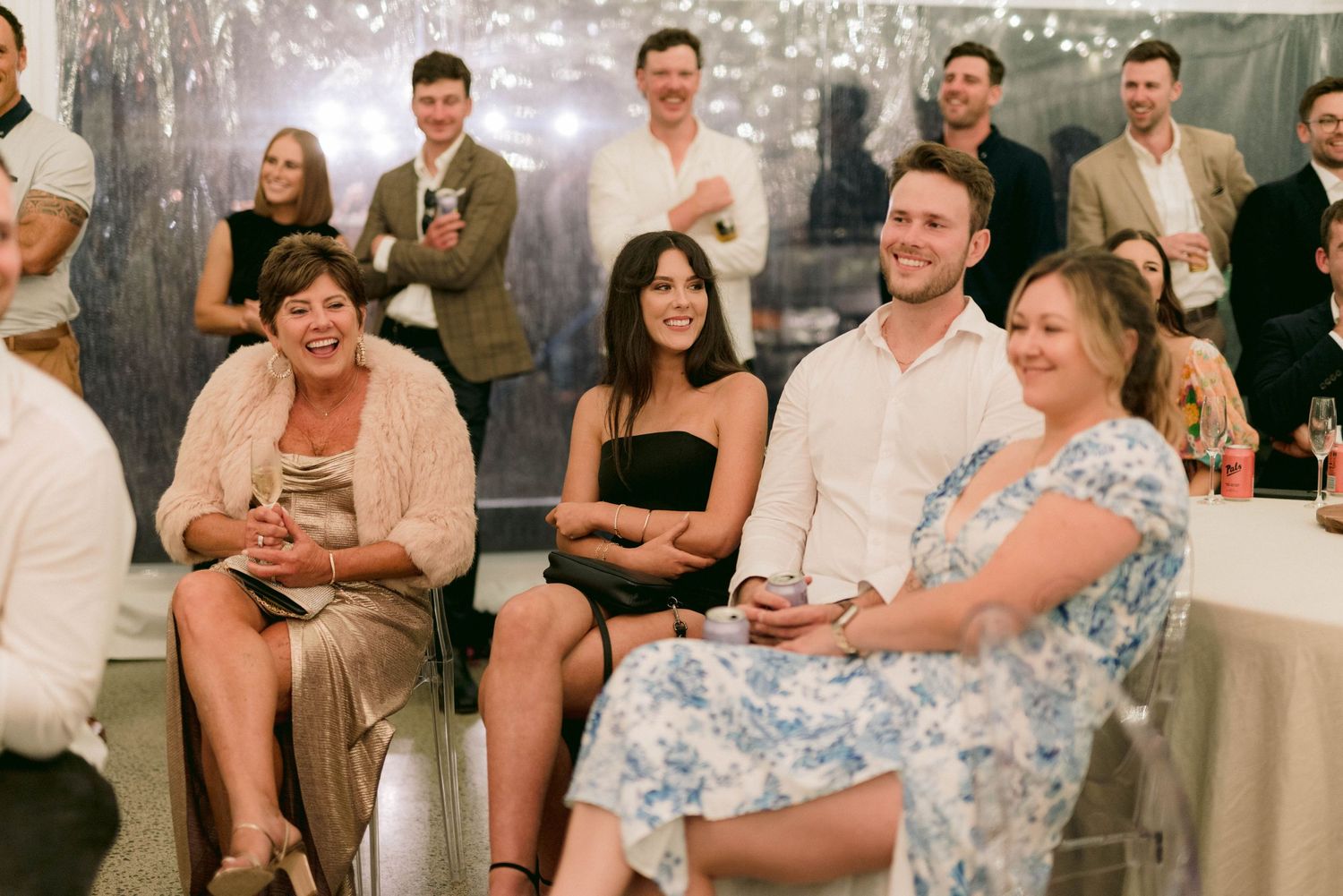 Wedding guests seated at round tables enjoy entertainment during an indoor reception.
