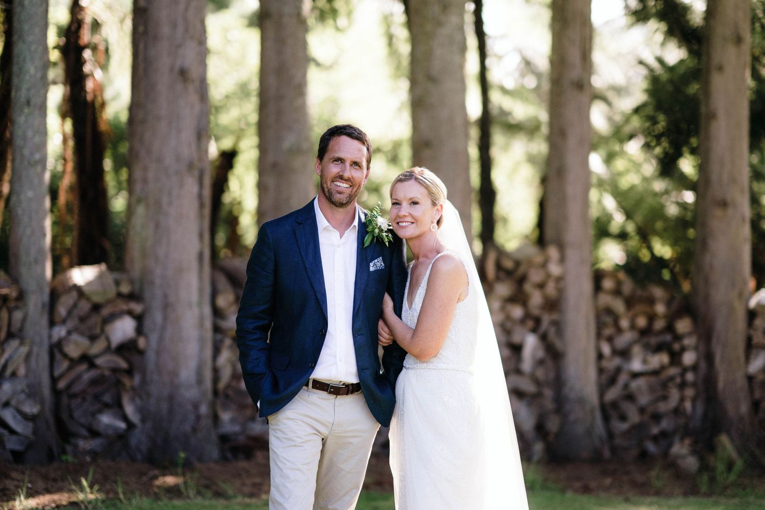 A wedding couple stands among tall trees in a forest setting on their special day.