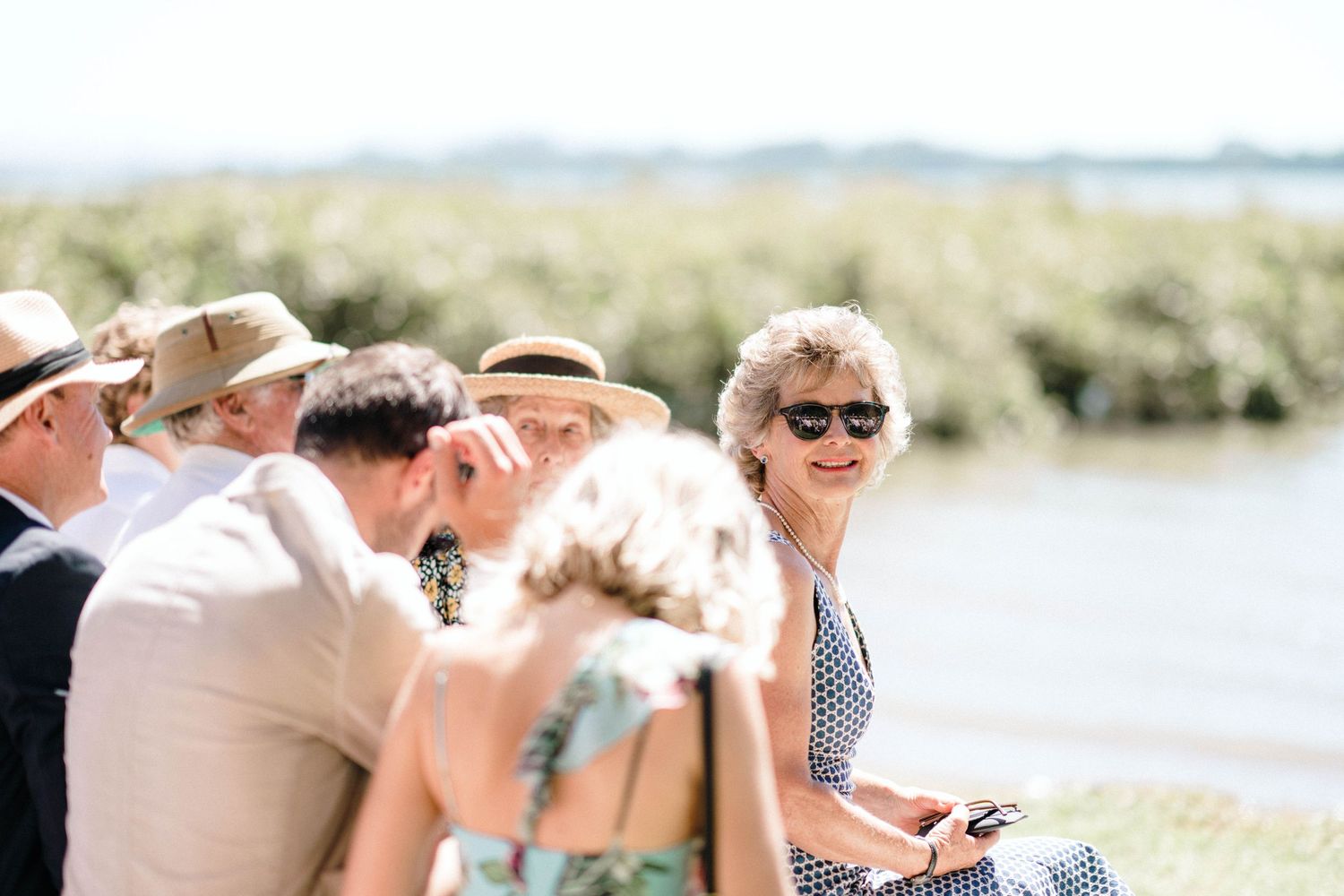 People in casual attire socialize at an outdoor gathering near a scenic lake or waterfront area.