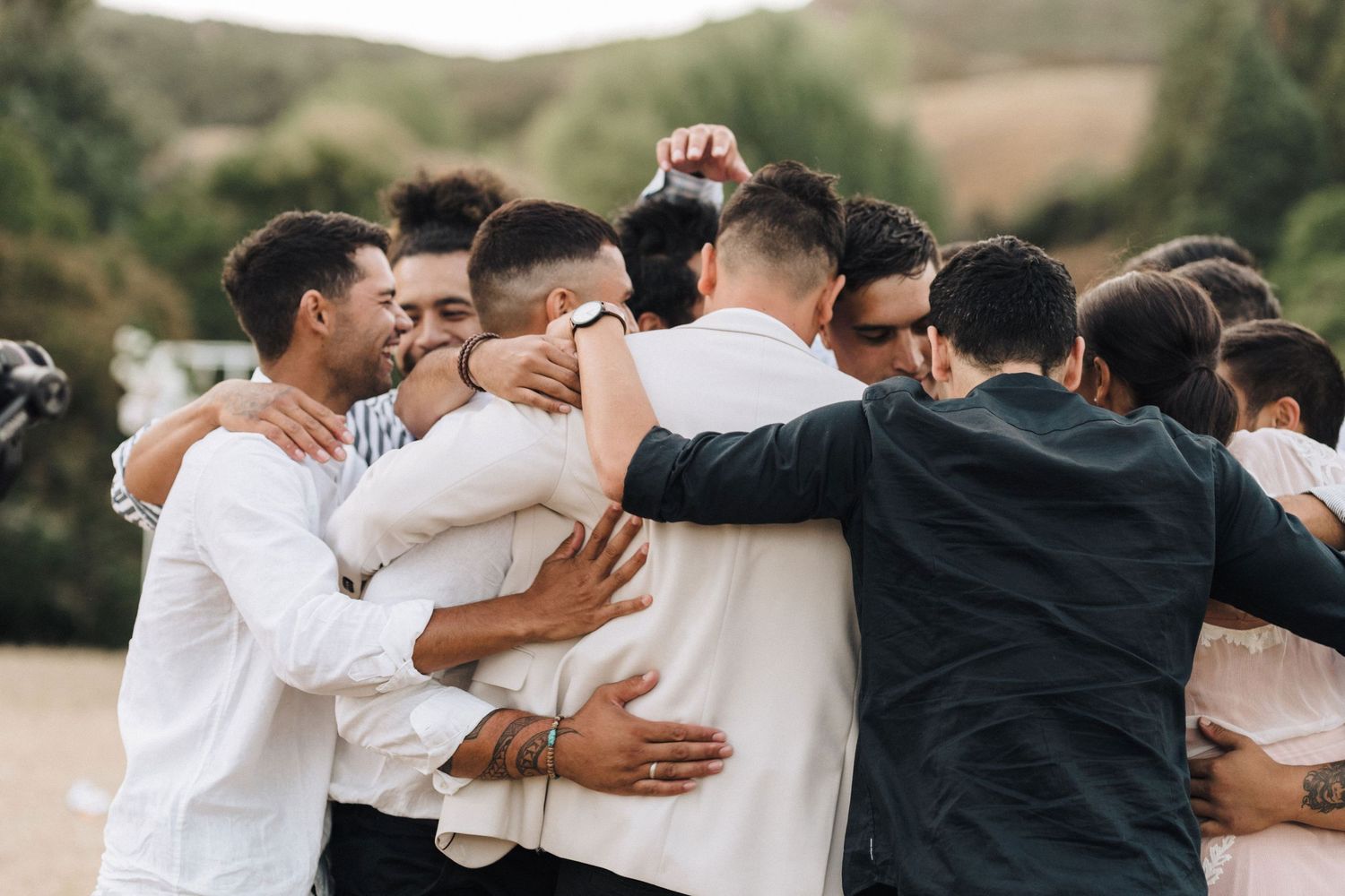Wedding guests embracing in a group huddle during outdoor celebration.