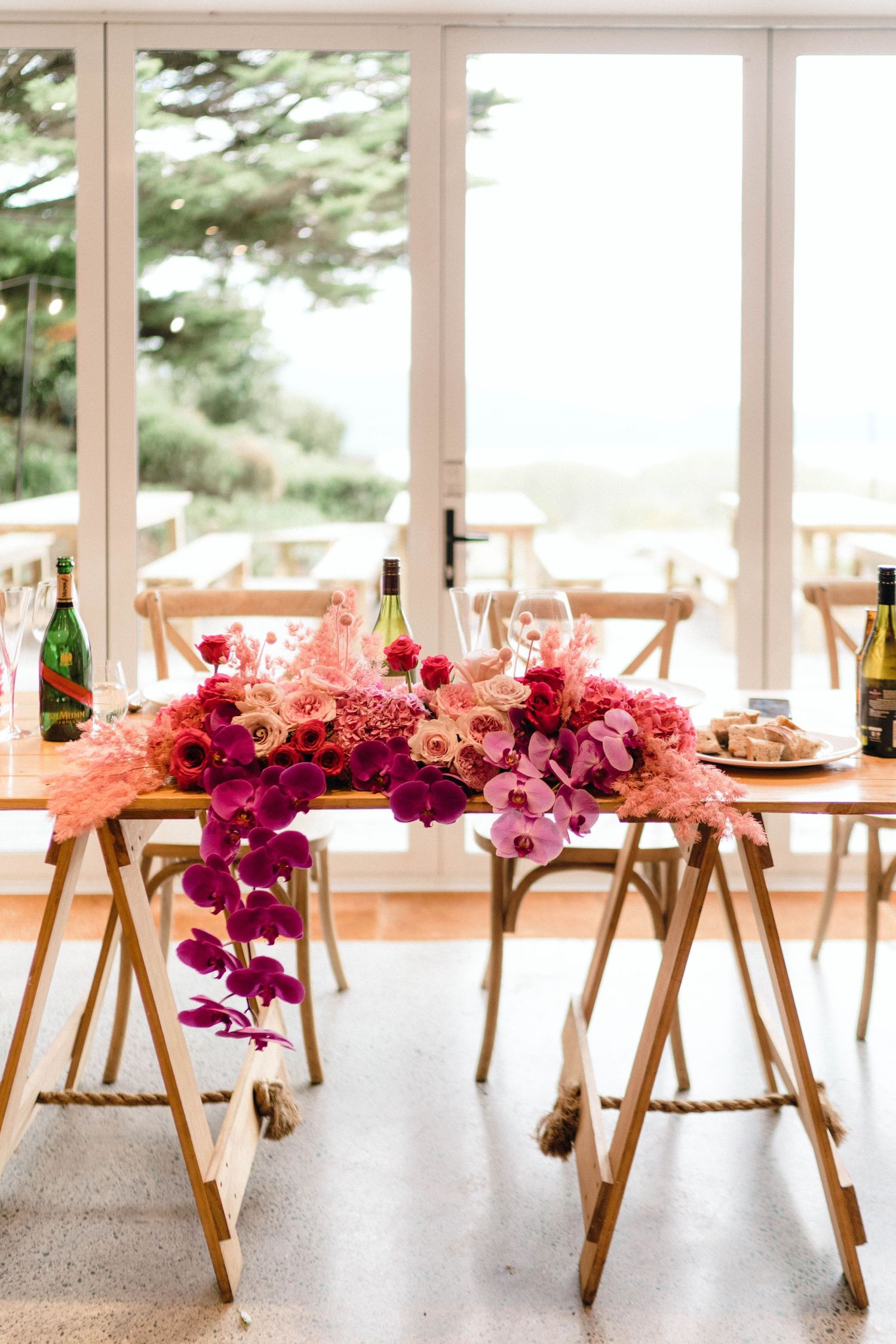 Elegant wedding table setting with vibrant pink and purple floral centerpiece against bright windows.