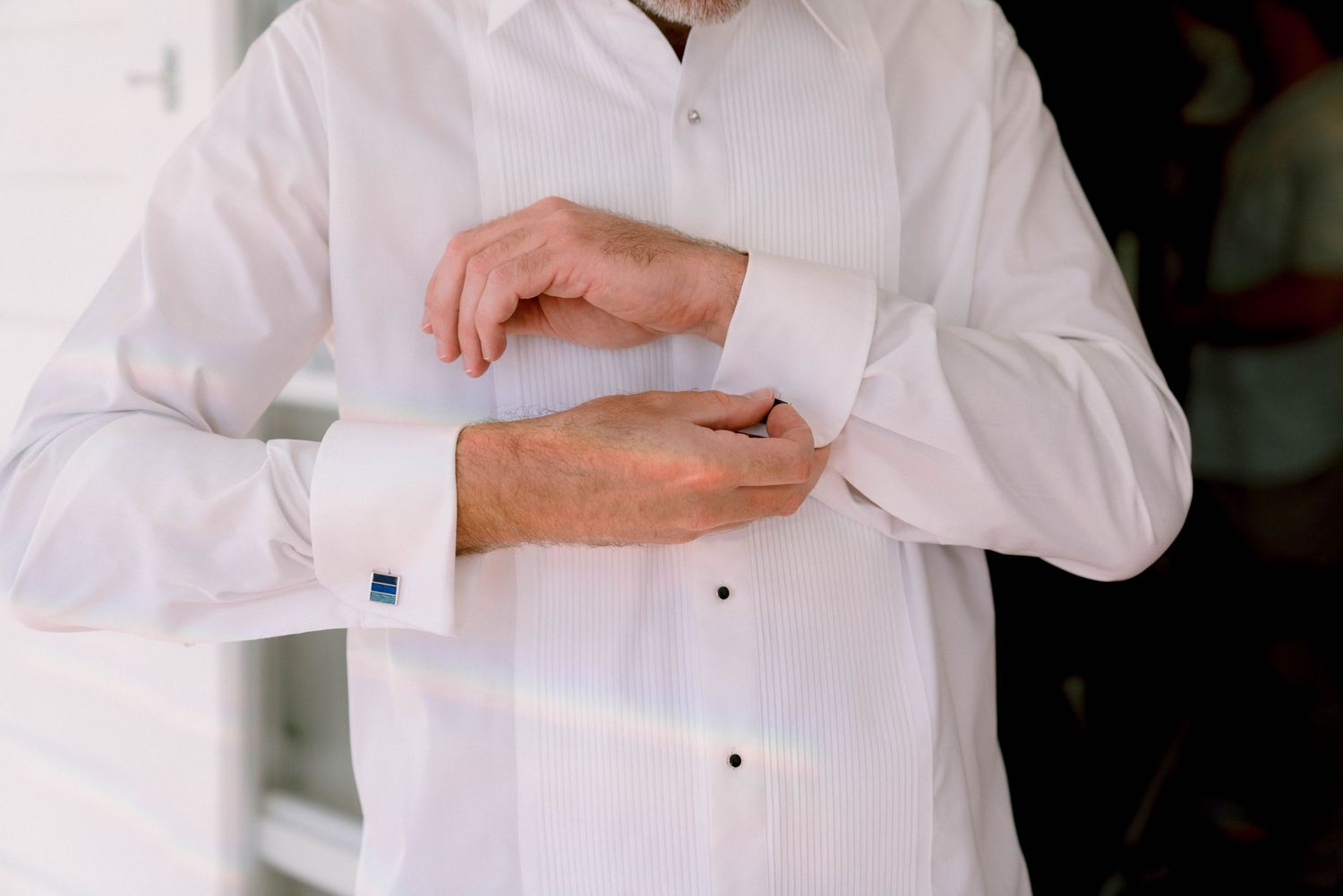 Person in crisp white dress shirt adjusting sleeve cuff with blue cufflink against dark background.