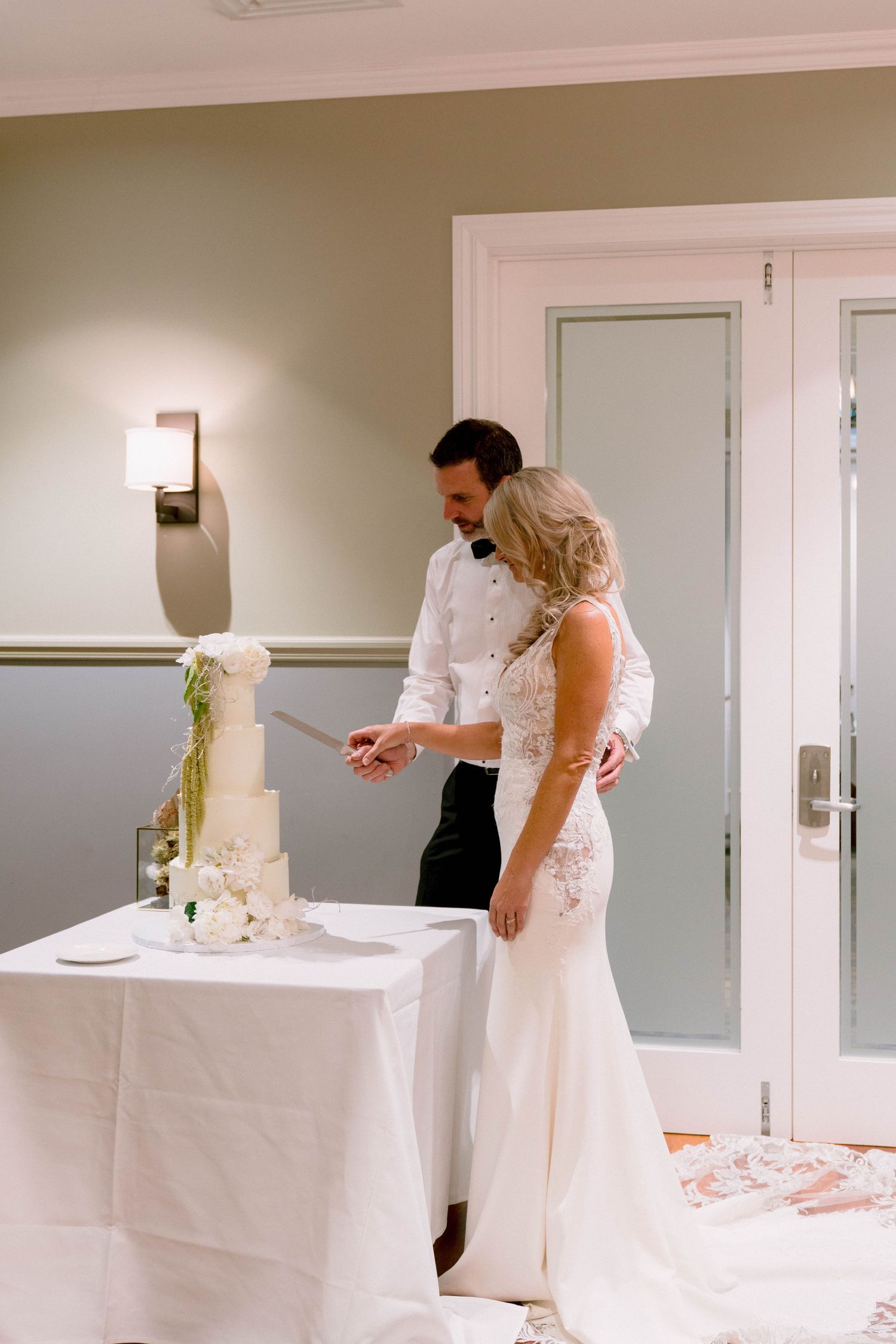 A couple cuts their elegant white wedding cake decorated with delicate flowers at their reception.