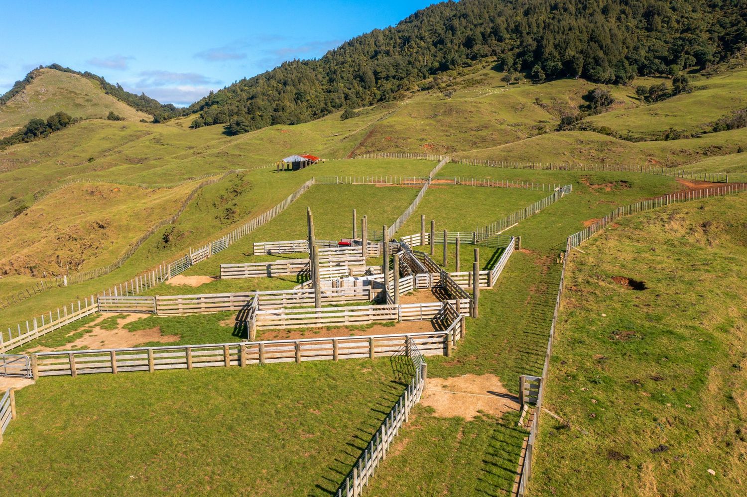 Ranch buildings and fences dot the hillside of a sprawling farm property with mountain views.