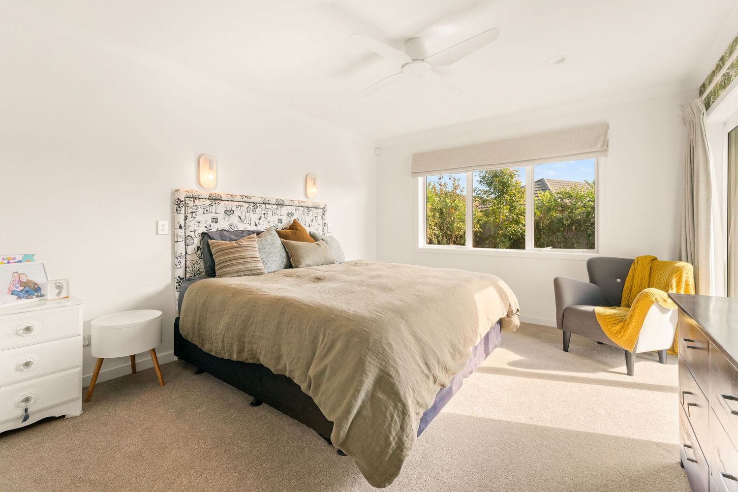 Master bedroom with gray bedding, yellow accent chair and large windows providing natural light.
