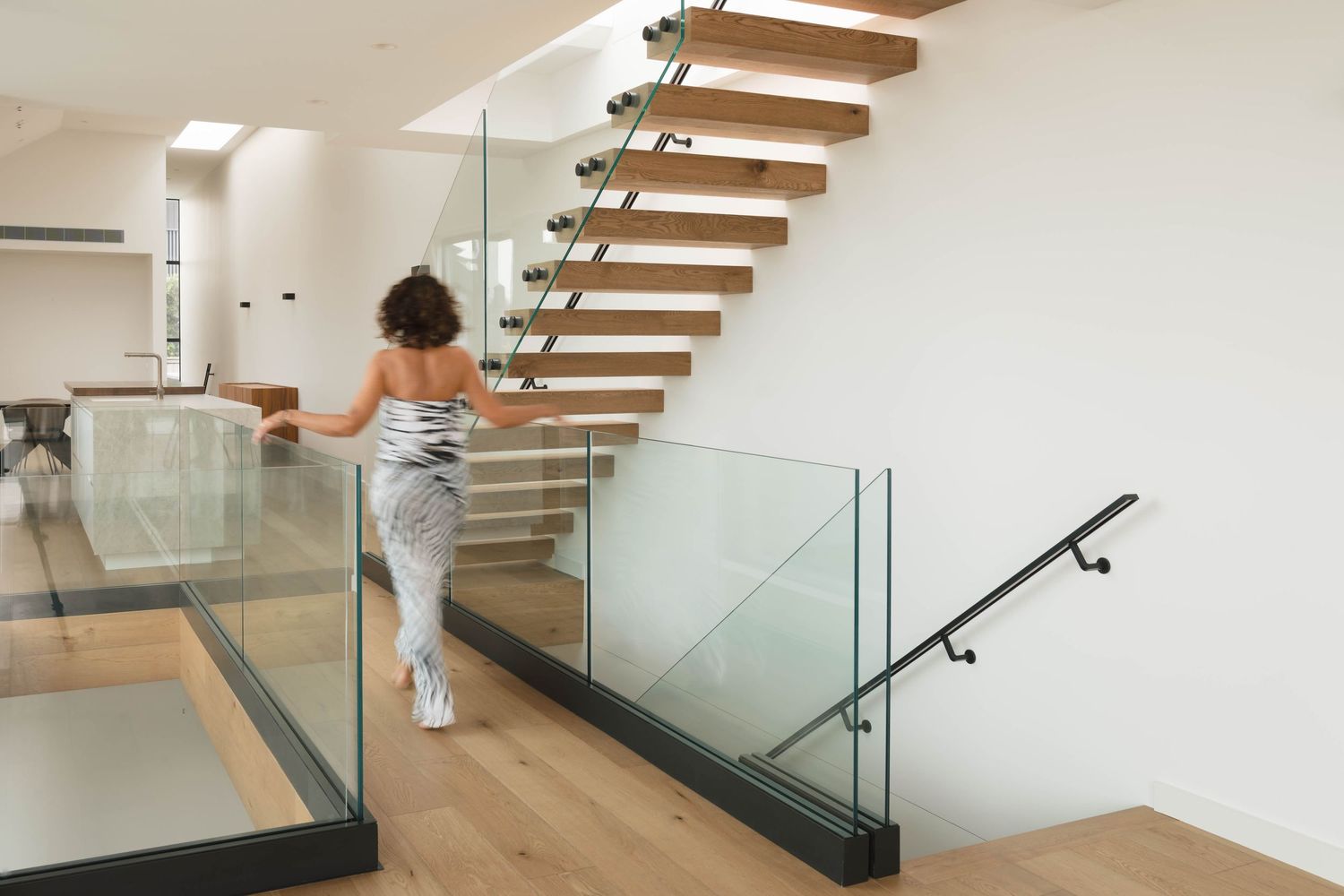 Modern floating wooden staircase with glass railings and white walls in a contemporary home interior.