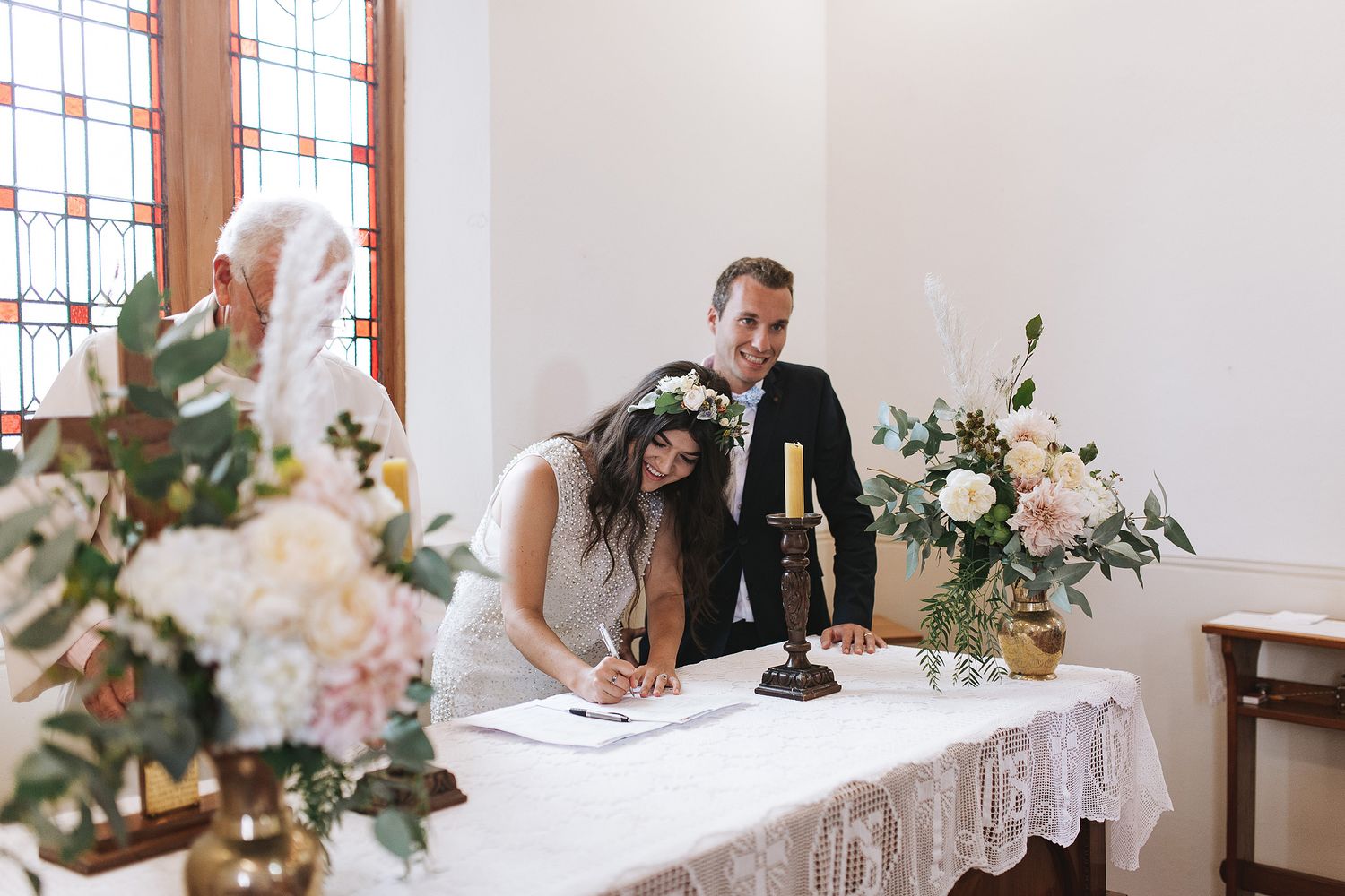 A couple signs their wedding document at a table decorated with delicate floral arrangements and white lace linens.