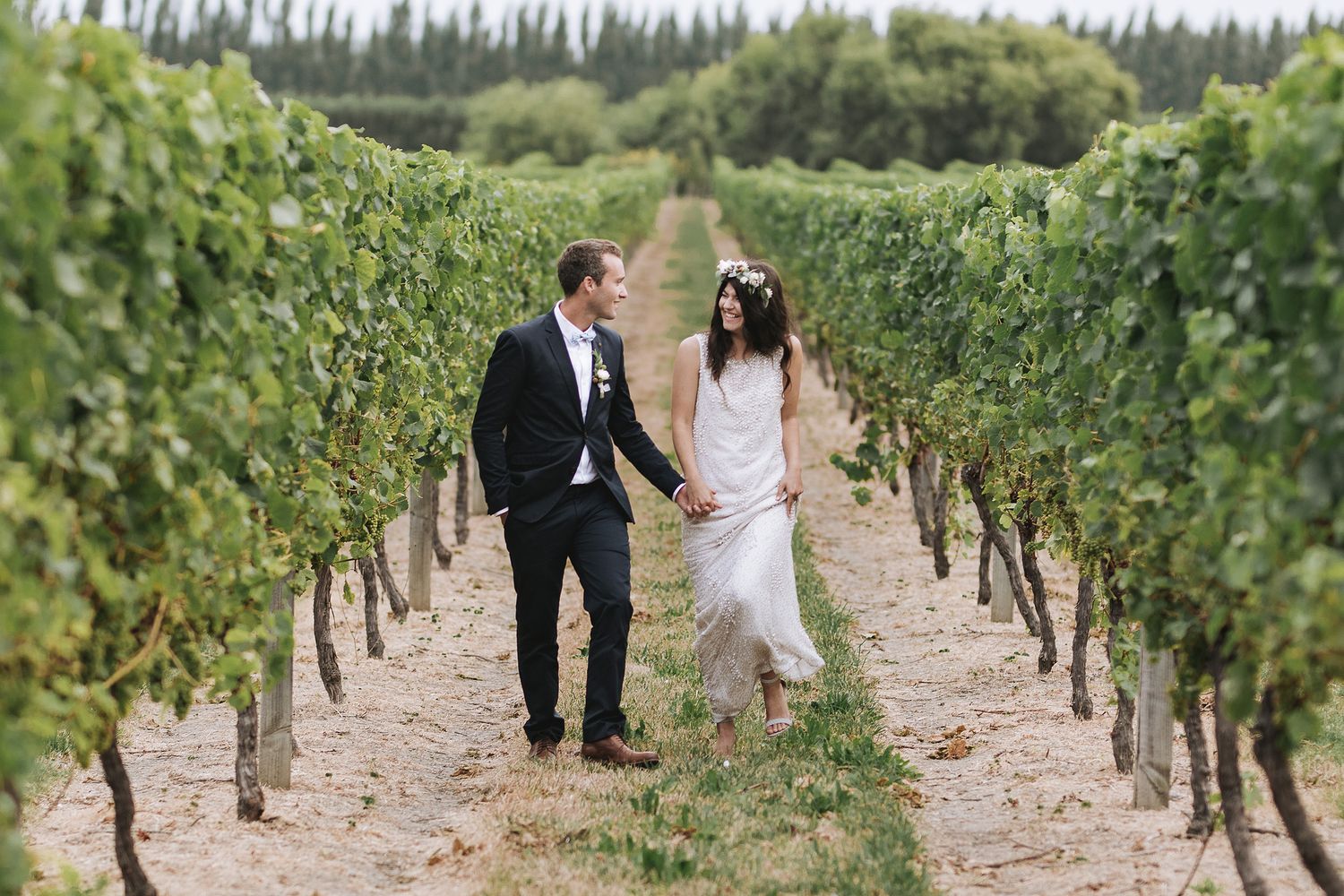 Couple strolls hand in hand through rows of grapevines in a scenic vineyard on a sunny day.