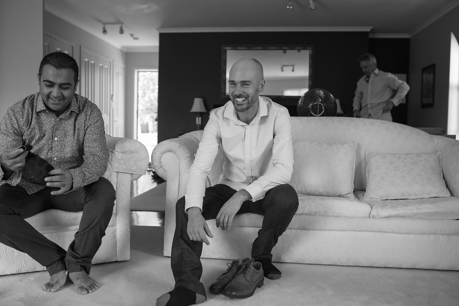 Black and white photo showing people relaxing in a living room with a white couch and ambient lighting.