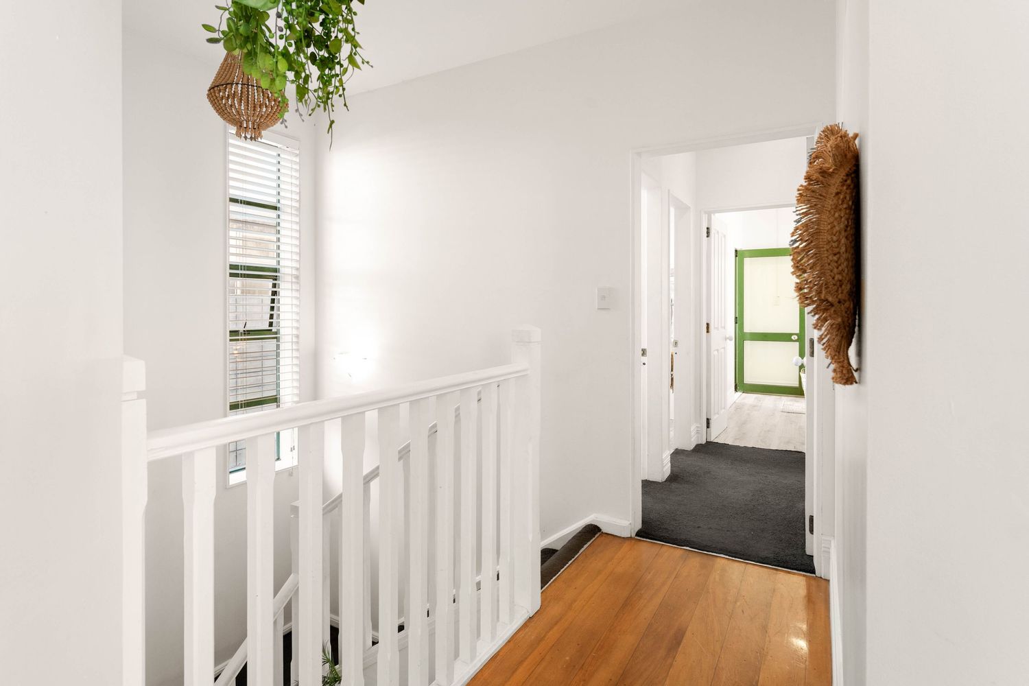 Bright hallway with white railings, hardwood floors, and hanging plants near window.
