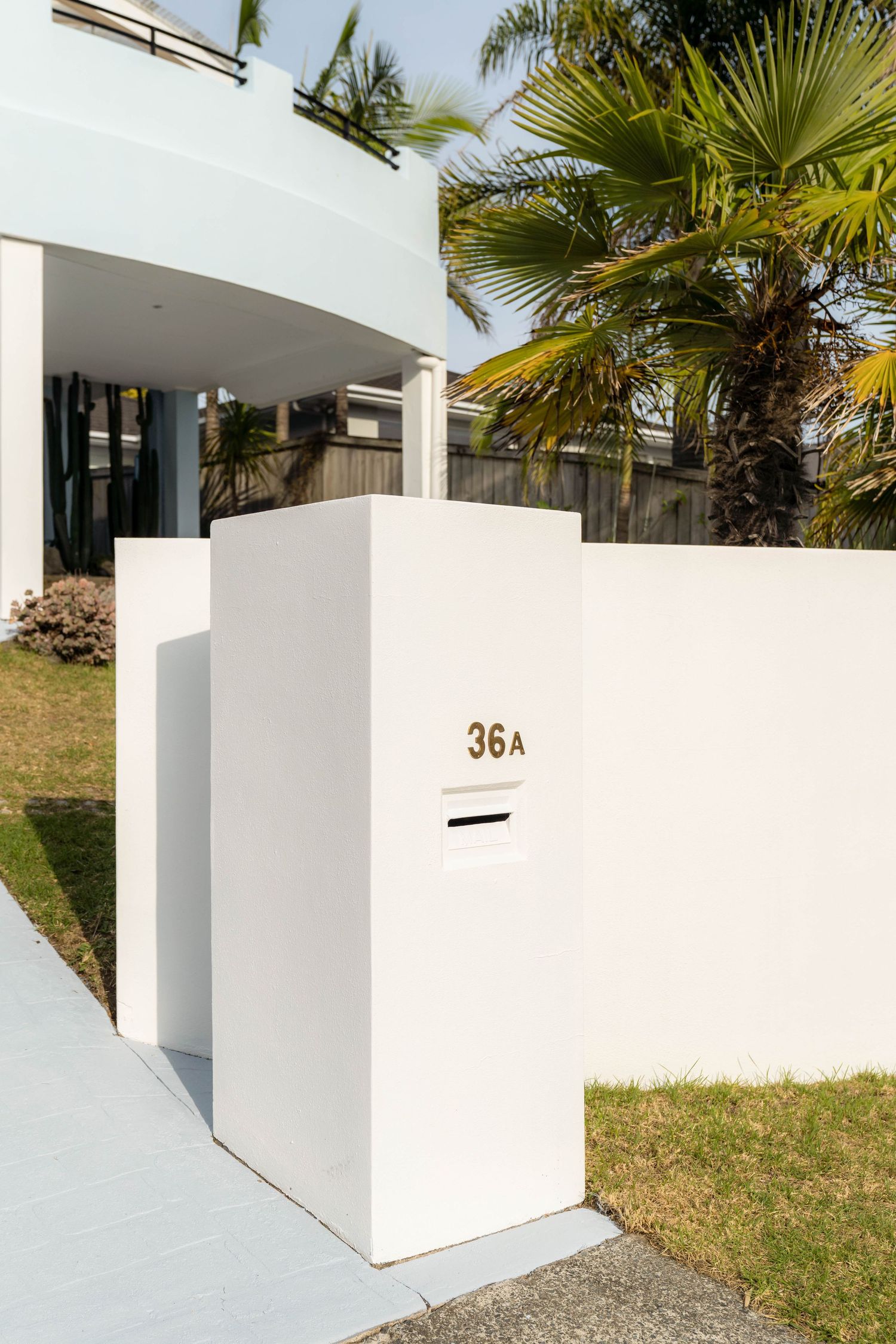 Modern white mailbox mounted on a sleek wall surrounded by tropical palm trees and landscaping.