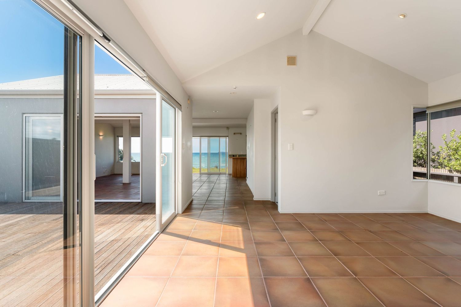Bright interior hallway with vaulted ceiling, sliding glass doors and terracotta flooring leading to outdoor deck.