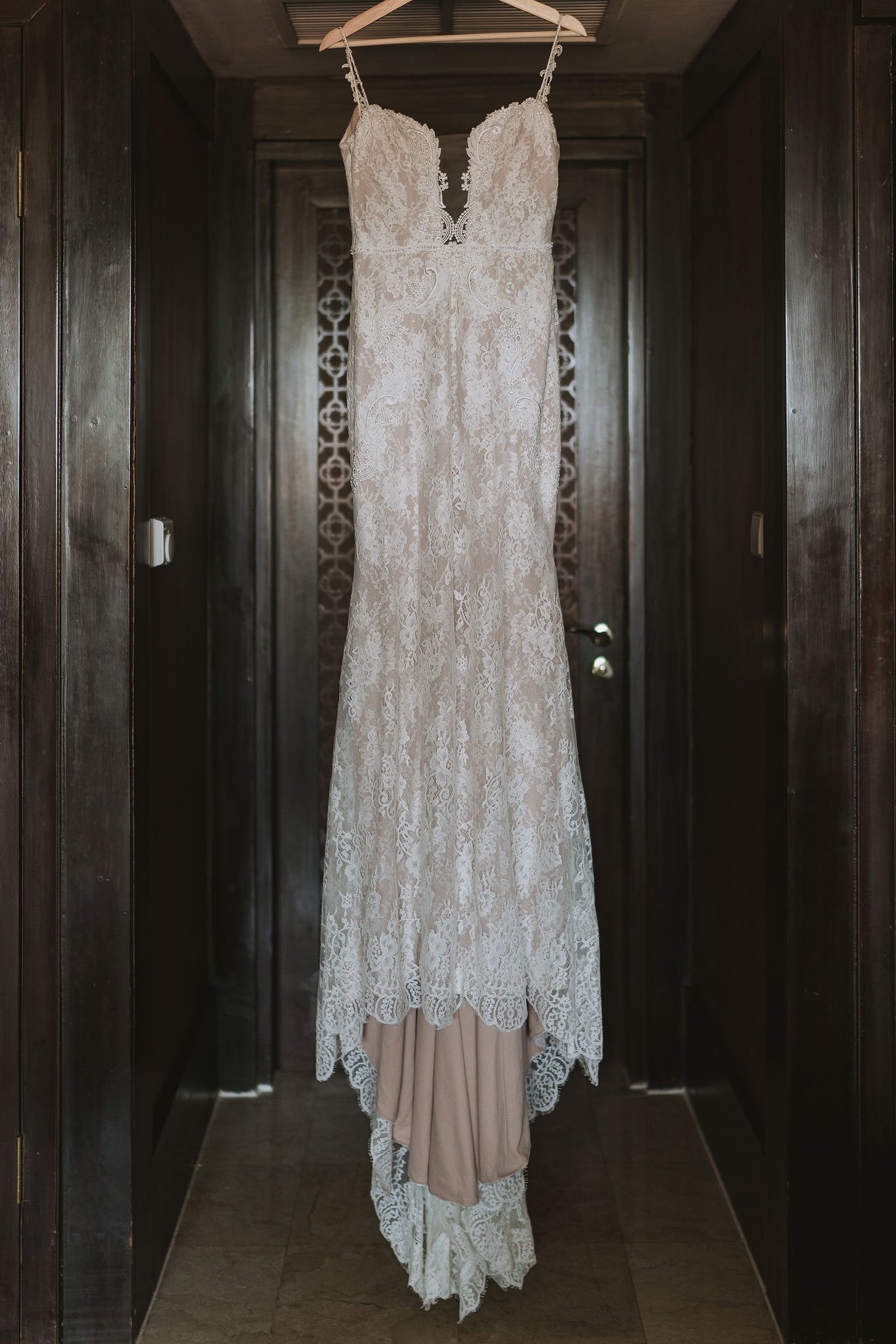 Elegant white lace wedding dress with sweetheart neckline hanging in dark hallway.