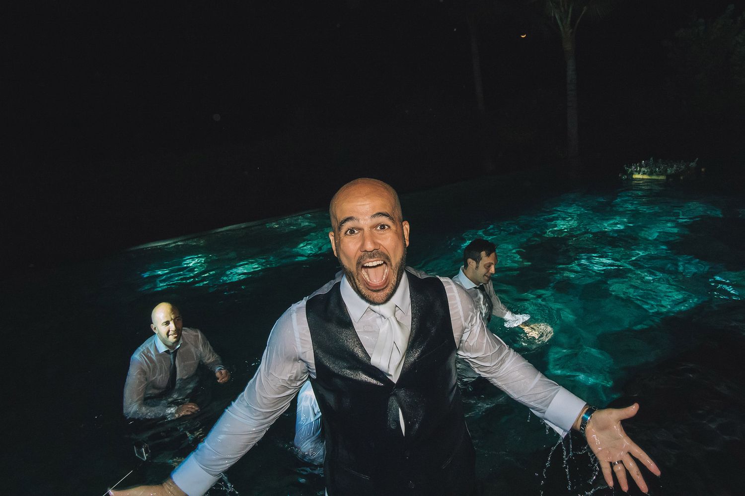 Man in formal attire gesturing animatedly on a dance floor with teal lighting effects.